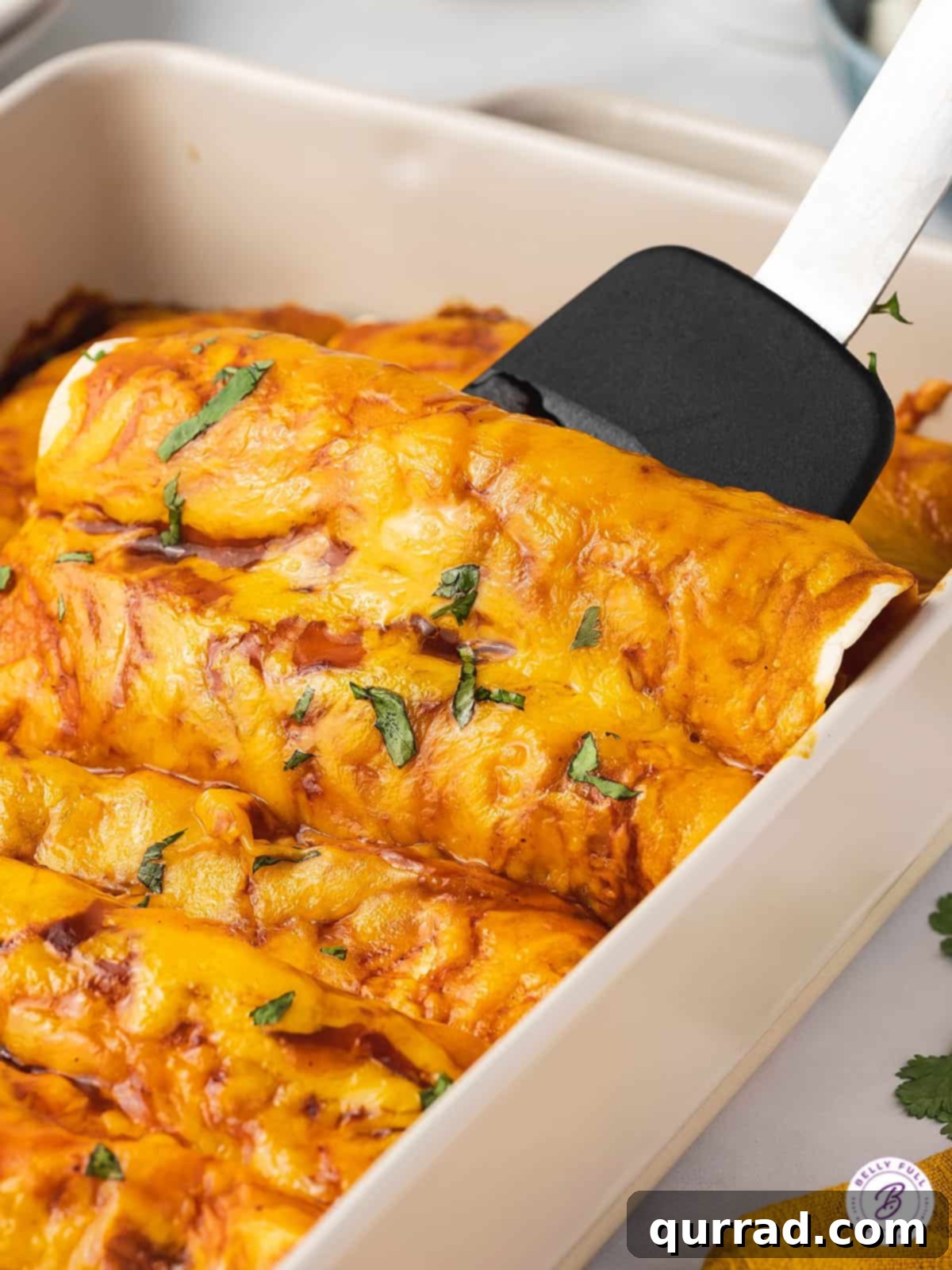 A spatula gently scooping a perfectly baked beef and rice enchilada from a bubbly casserole dish, ready to be served.