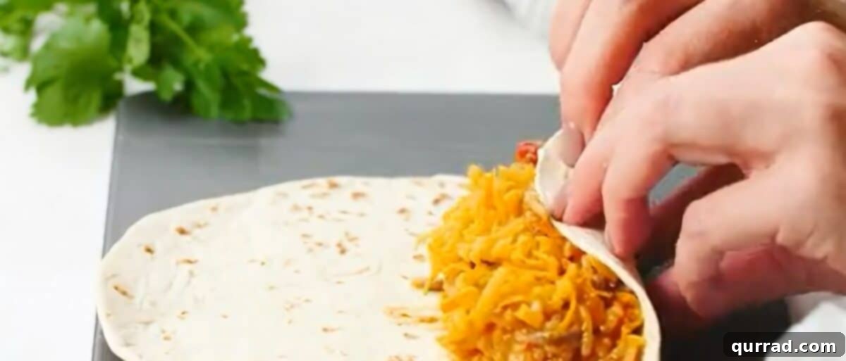 Rolling up a flour tortilla filled with the beef and rice mixture and shredded cheese on a clean work surface.