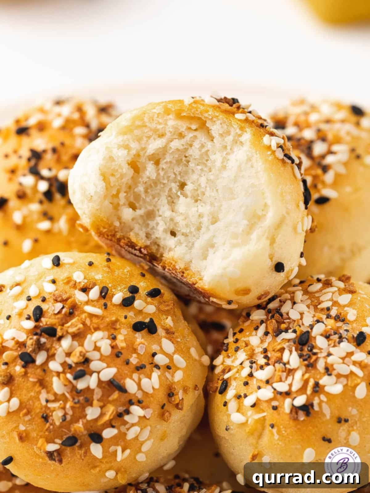 Freshly Made Air Fryer Bagel Minis A stack of perfectly air-fried bagel balls, one with a bite missing, showcasing the delicious interior, presented on a white background.