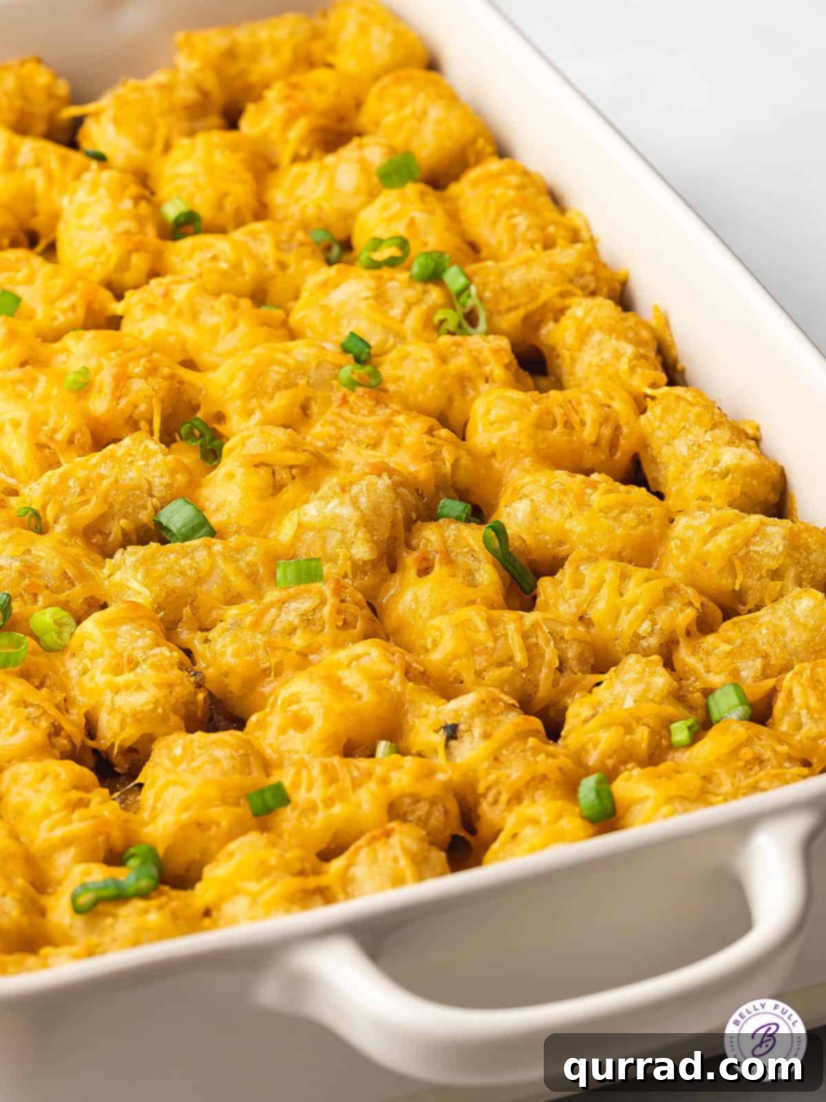 Made with ground beef, tater tots, cheese, frozen veggies, and soup, this Cheeseburger Tater Tot Casserole makes a quick and easy dinner. Overhead view of half of a tater tot cheeseburger casserole, displaying its layers and rich texture.