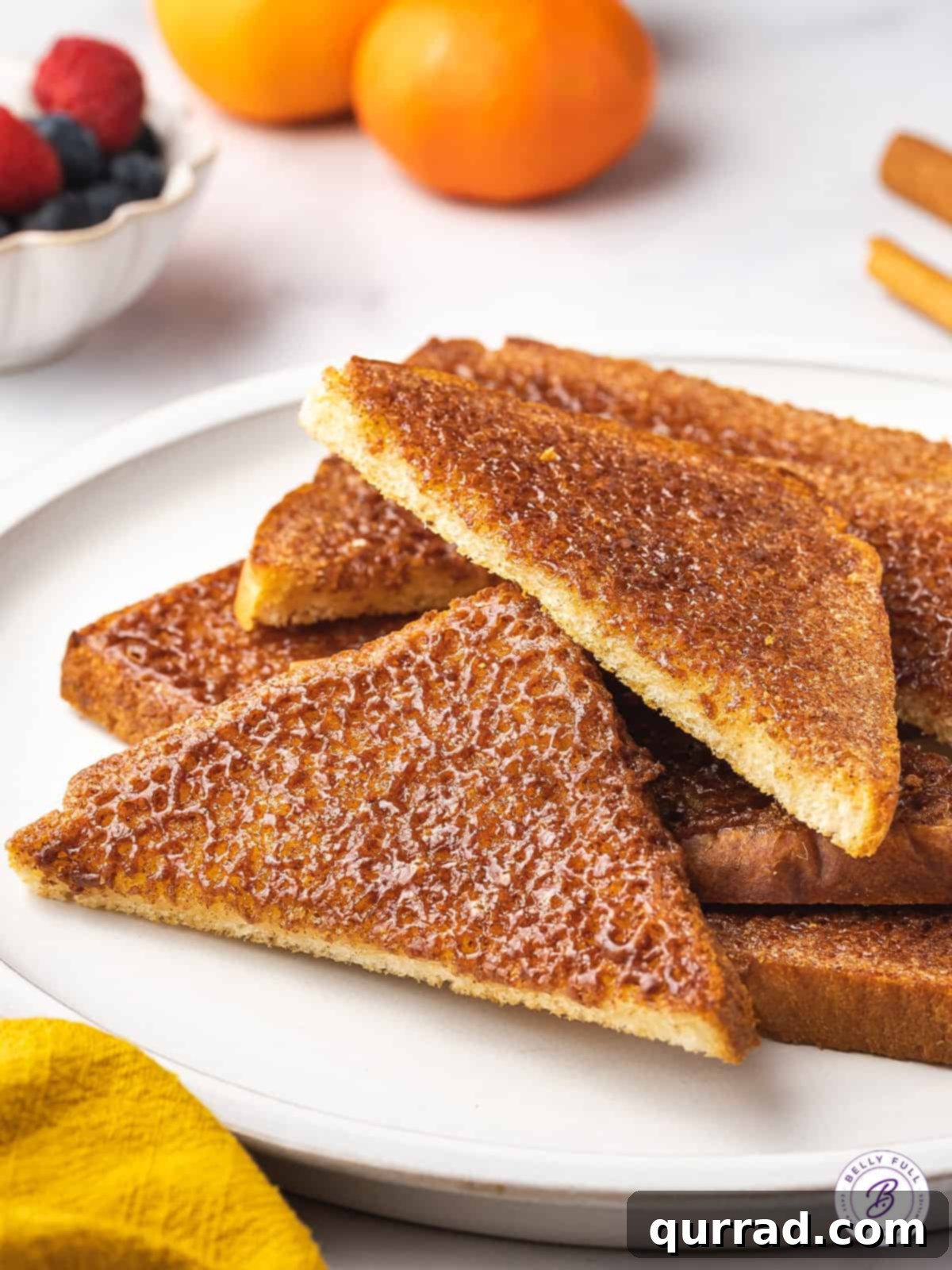 Diagonal halves of perfectly caramelized cinnamon sugar toast on a pristine white plate, showcasing its golden crust and inviting texture.