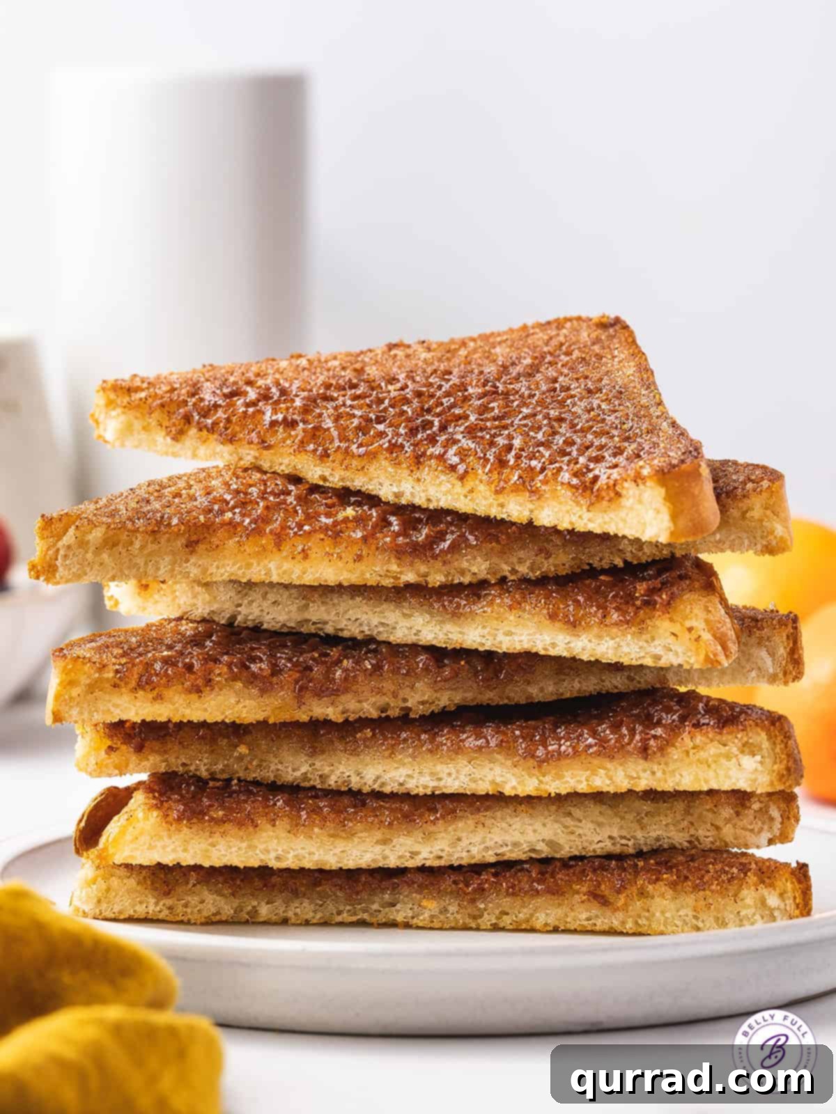 A beautifully arranged stack of cinnamon toast halves on a white plate, showcasing the crispy edges and golden brown topping, inviting a delicious bite.