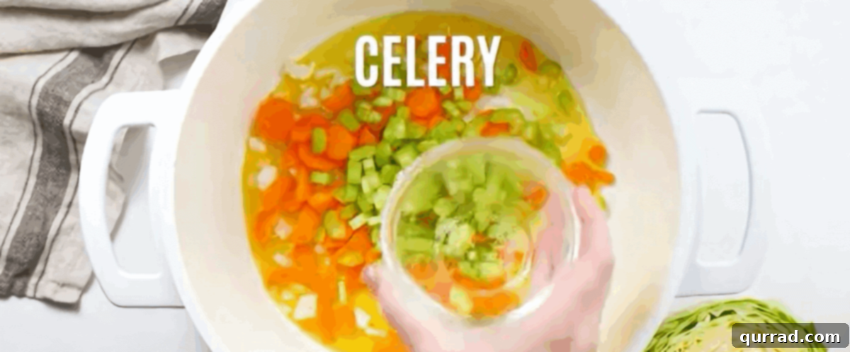 Hearty Cabbage Comfort 3 The initial stage of cooking, showing diced onions, carrots, and celery sautéing in olive oil in a large white pot until tender and fragrant.
