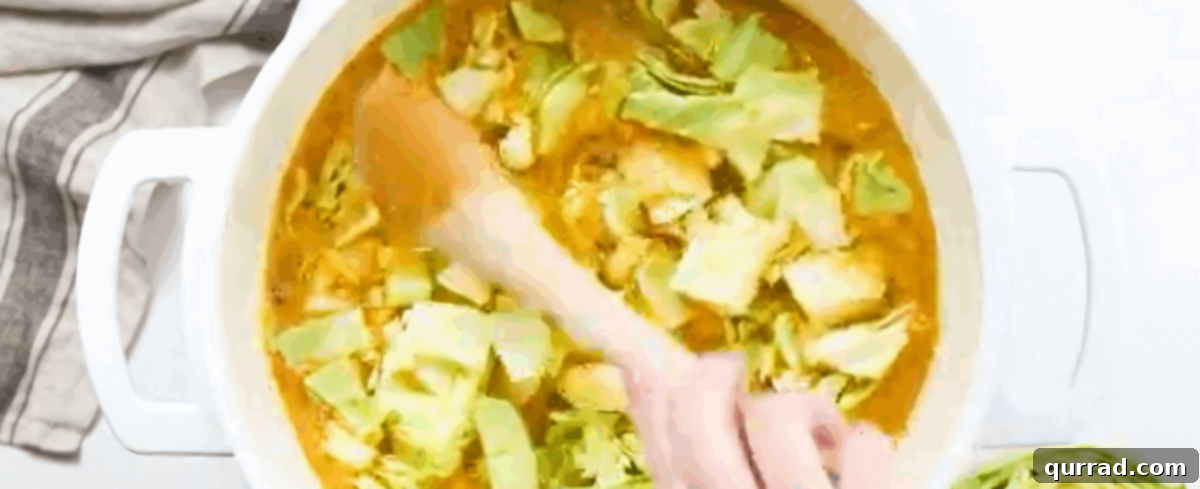Hearty Cabbage Comfort 4 Freshly chopped cabbage being added to a pot already containing sautéed vegetables and simmering broth, ready to wilt down.