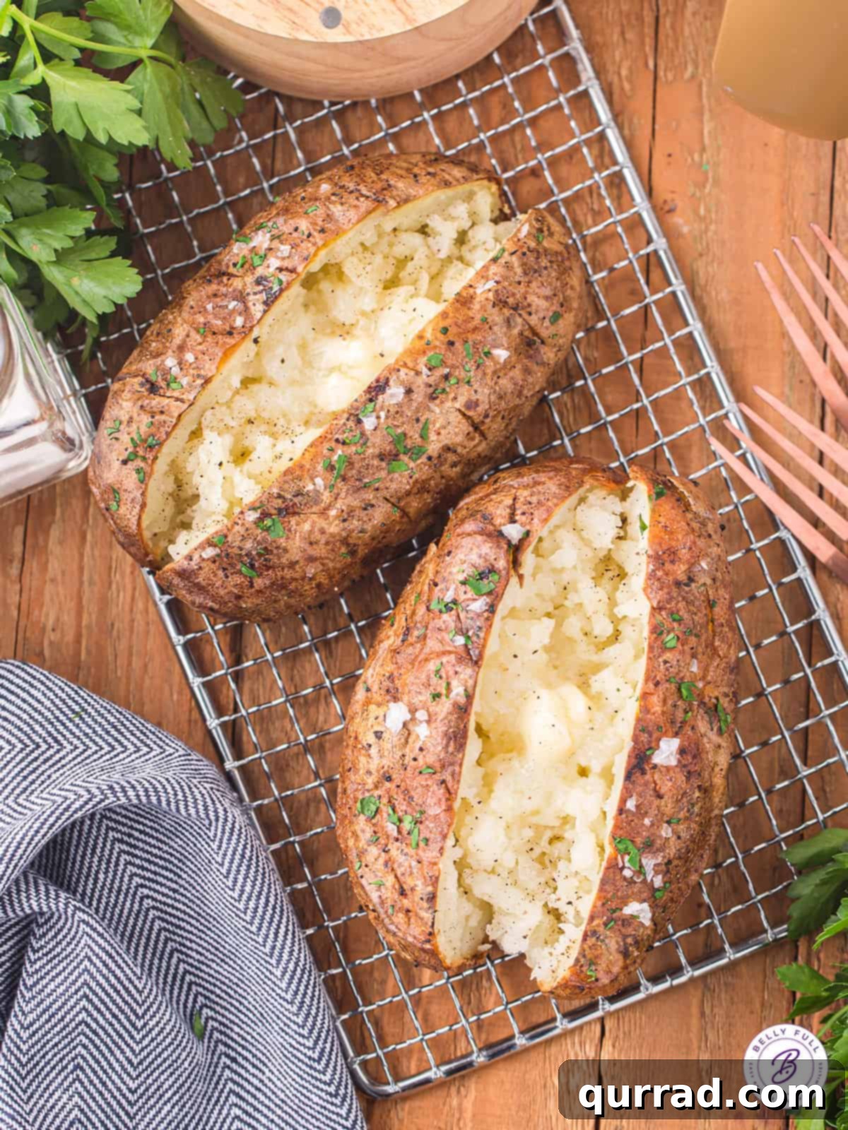 These Air Fryer Baked Potatoes are delicious, easy and don’t require you to heat your oven! Just a few simple steps & even fewer ingredients! Two perfectly baked potatoes, golden and crisp, resting on a cooling rack, ready to be topped and enjoyed.