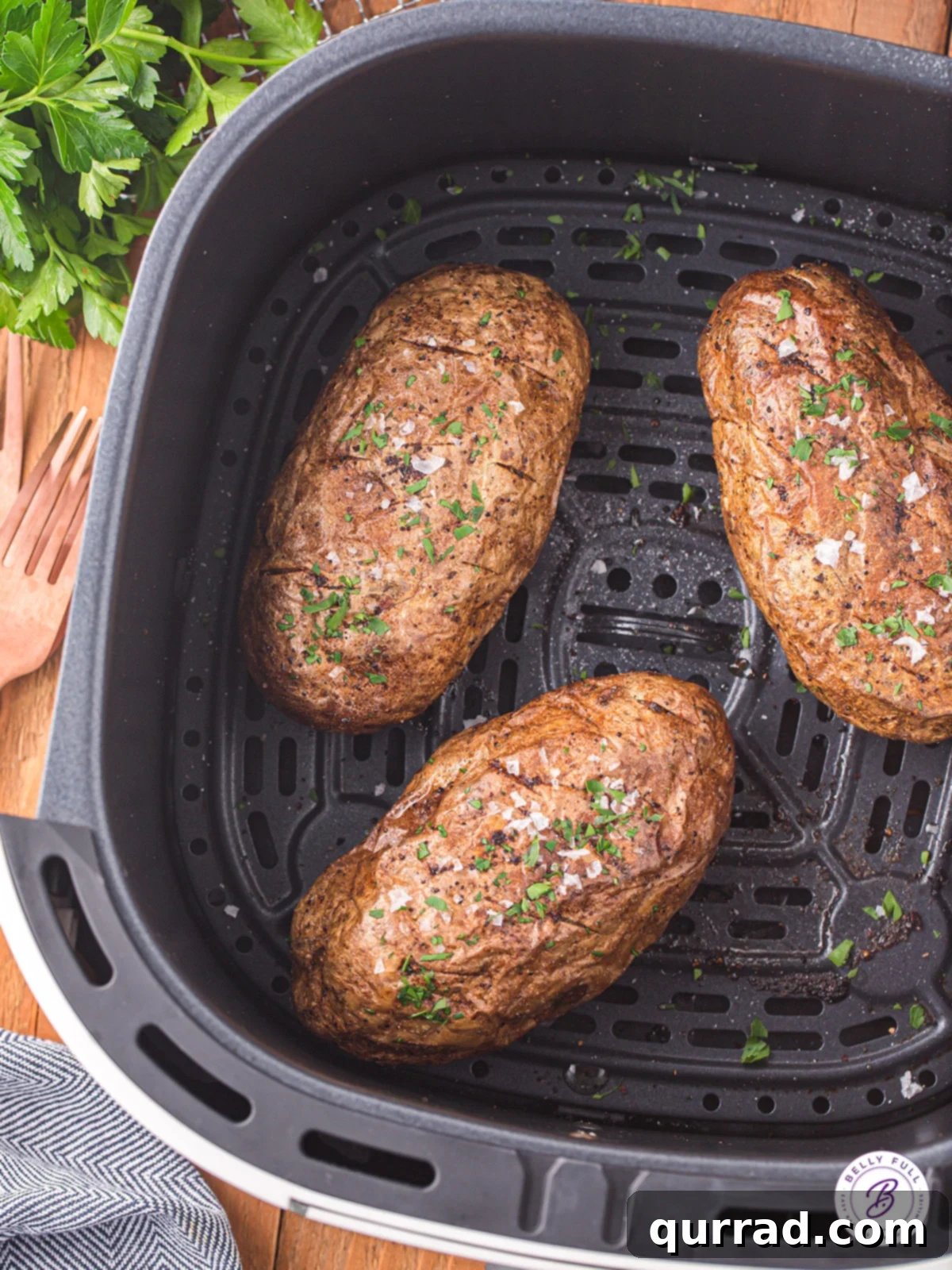 These Air Fryer Baked Potatoes are delicious, easy and don’t require you to heat your oven! Just a few simple steps & even fewer ingredients! Three perfectly seasoned Russet potatoes nestled in an air fryer basket, ready for cooking to achieve a crispy exterior and fluffy interior.