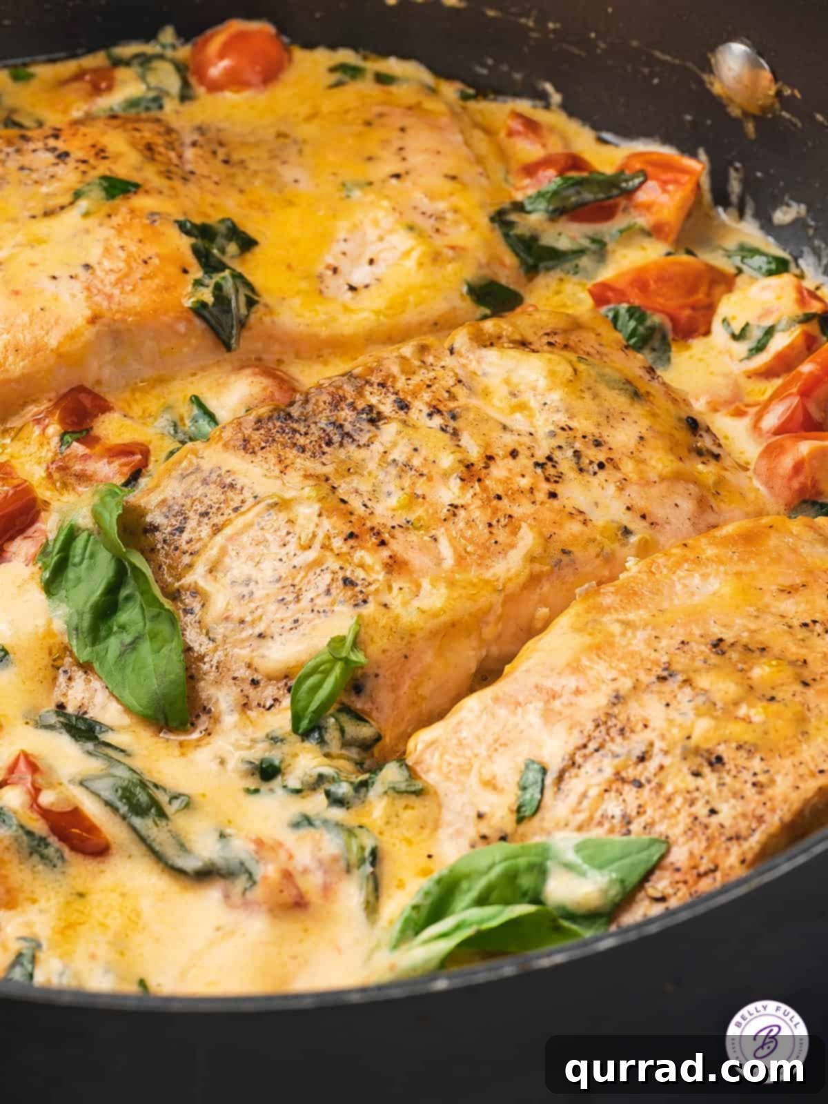 This Tuscan Butter Salmon recipe is super easy to make, but tastes like something you'd order at a 5-star restaurant! Ready in 30 minutes! Close-up of perfectly pan-seared Tuscan Butter Salmon with creamy sauce, cherry tomatoes, and spinach