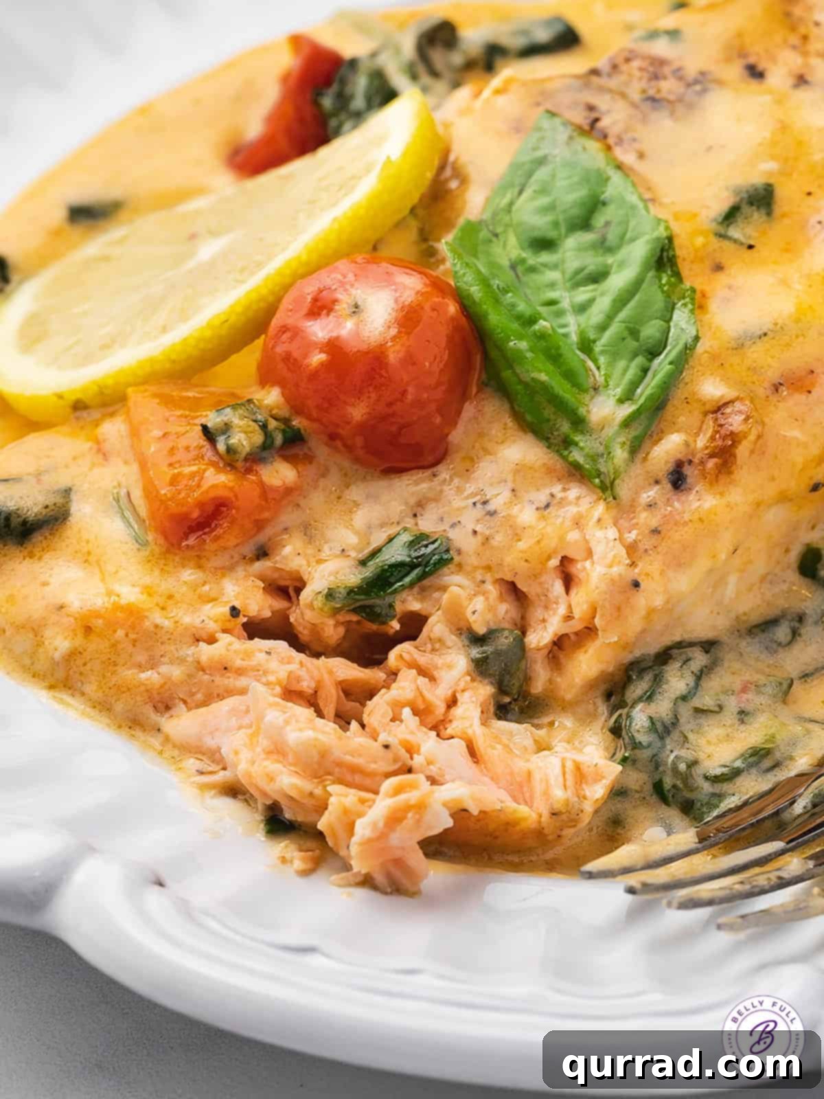 This Tuscan Butter Salmon recipe is super easy to make, but tastes like something you'd order at a 5-star restaurant! Ready in 30 minutes! Close-up of creamy Tuscan salmon on a white plate with fresh herbs