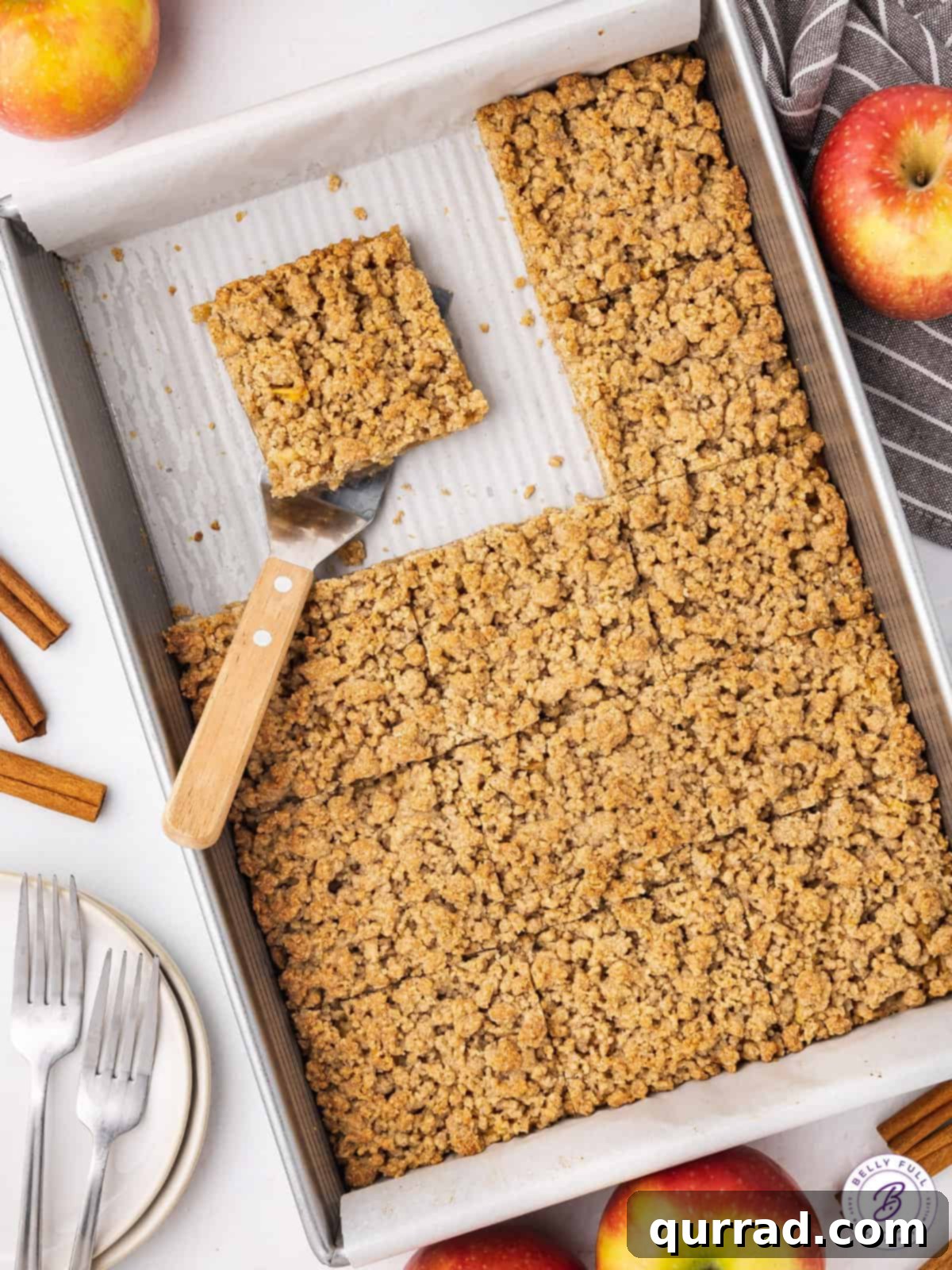 Apple Crumble Bars 10 A rectangular baking pan filled with neatly cut apple pie bars, some servings already removed, showcasing their even layers and golden crumble tops.