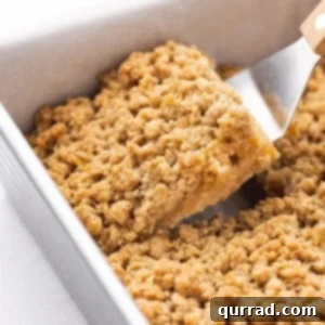 A single apple crumble square being carefully lifted from a baking pan, showcasing its perfect shape and golden topping.