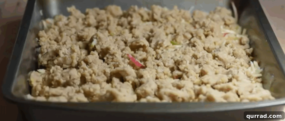 Apple Crumble Bars 7 A baking pan filled with assembled apple pie bars, showing the bottom crumble layer, the apple filling, and the top crumble layer sprinkled over, ready for baking.