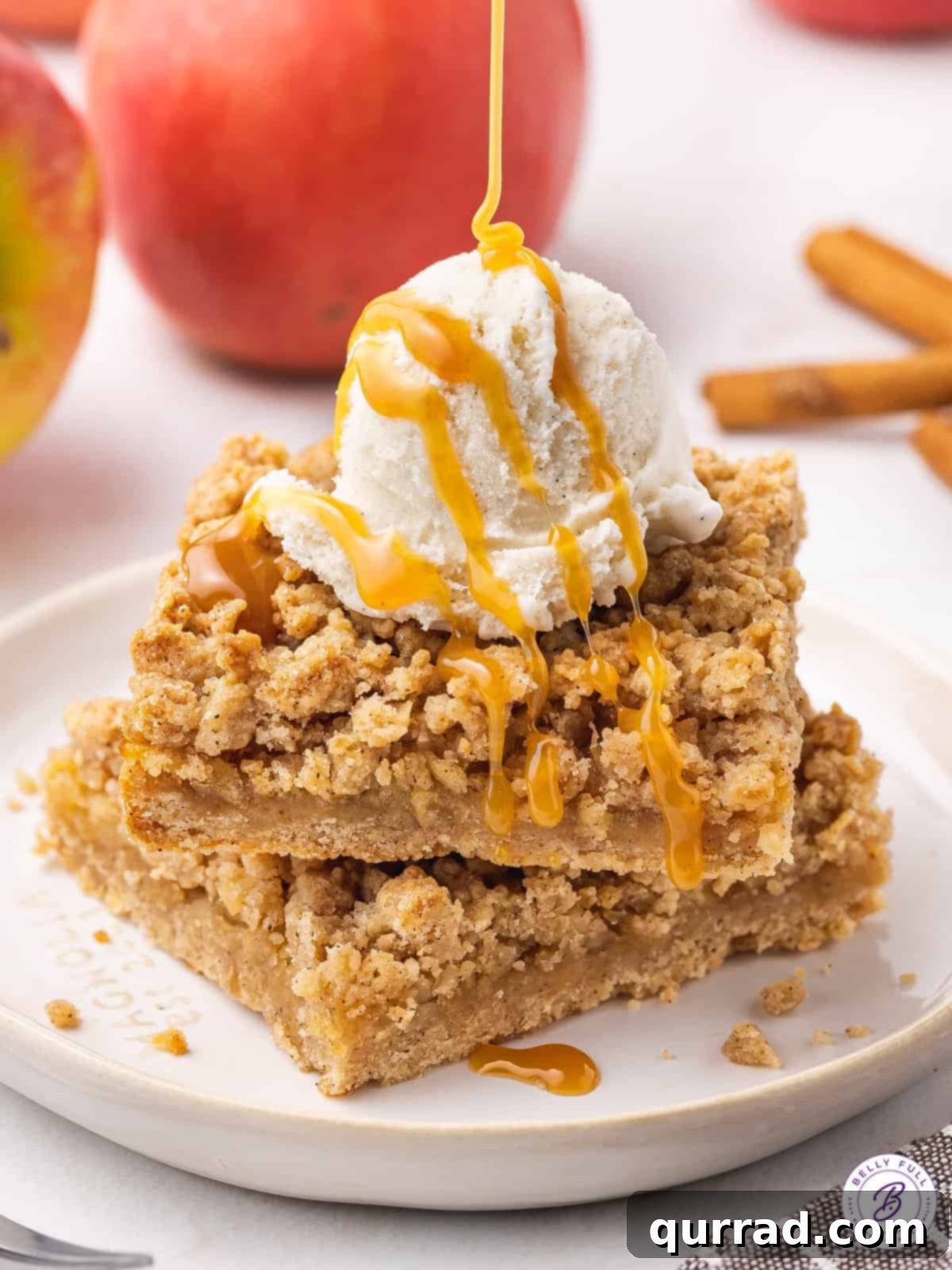 Apple Crumble Bars 8 Two freshly baked apple pie bars stacked on a plate, generously topped with a scoop of vanilla ice cream and a drizzle of rich caramel sauce, ready to be enjoyed as a decadent dessert.