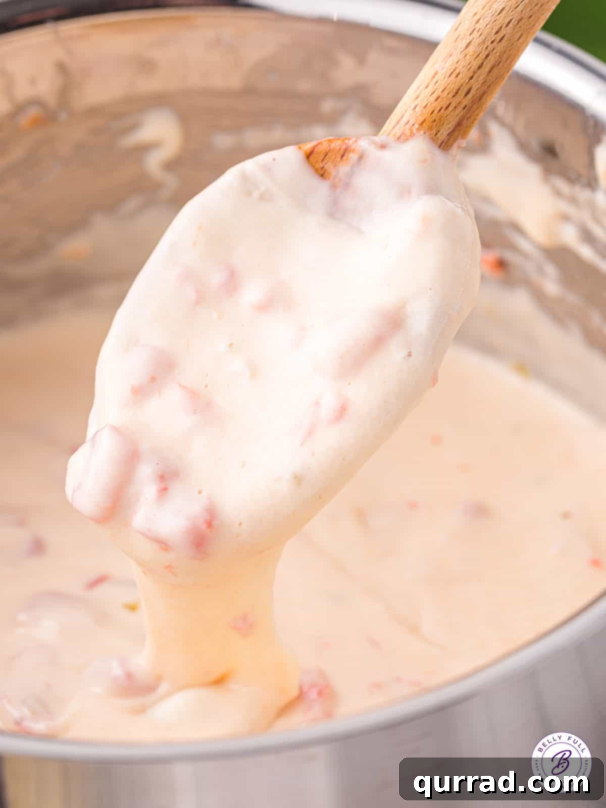A wooden spoon gently stirring a pot of molten, creamy queso blanco dip, highlighting its smooth texture.