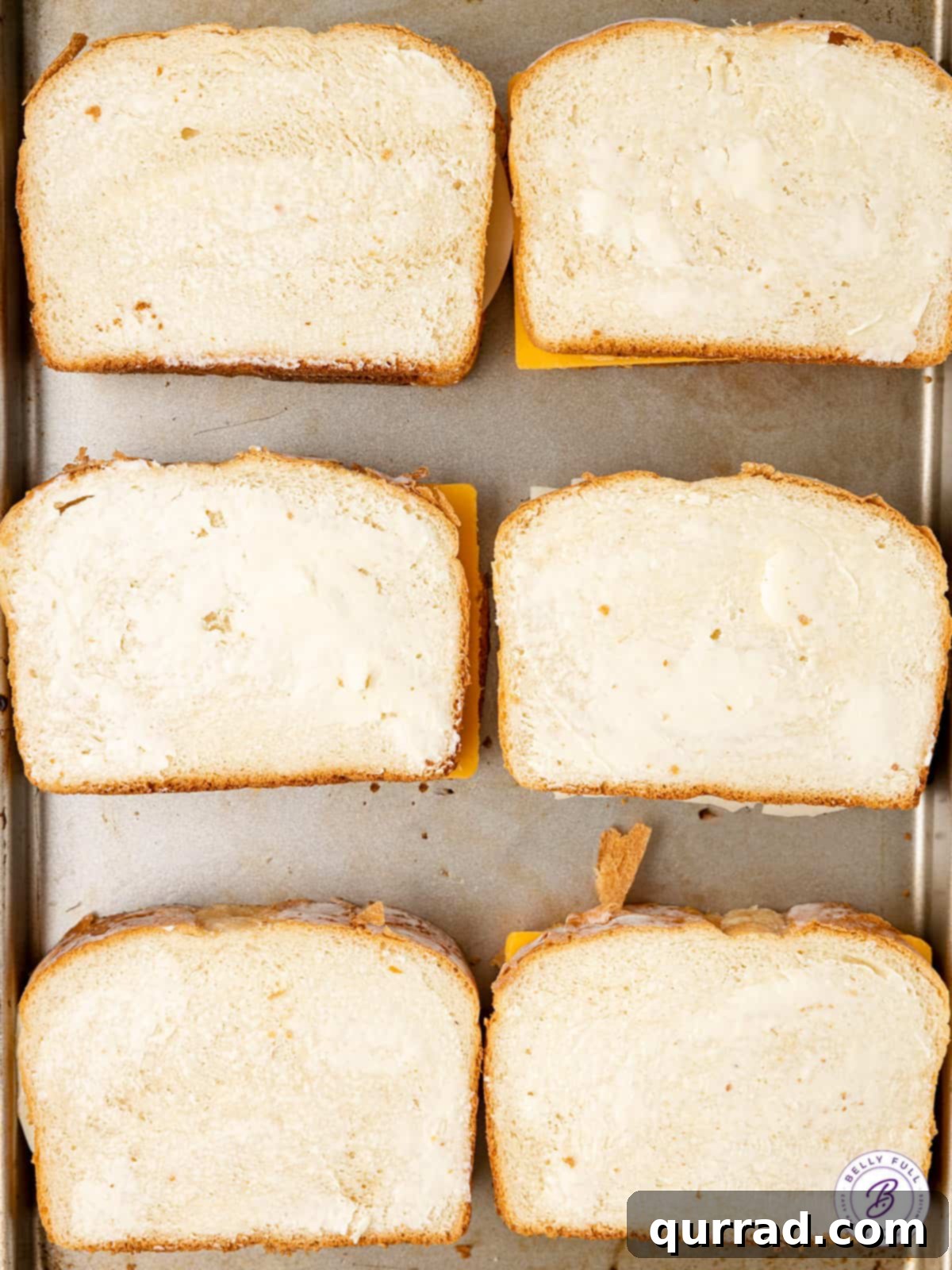 Slices of bread buttered and ready for cheese on a baking sheet for oven grilled cheese