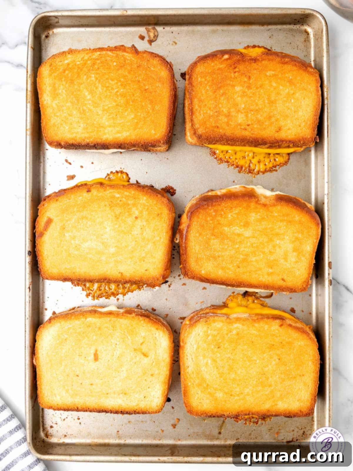 Overhead view of several golden-brown sheet pan grilled cheese sandwiches on a baking sheet