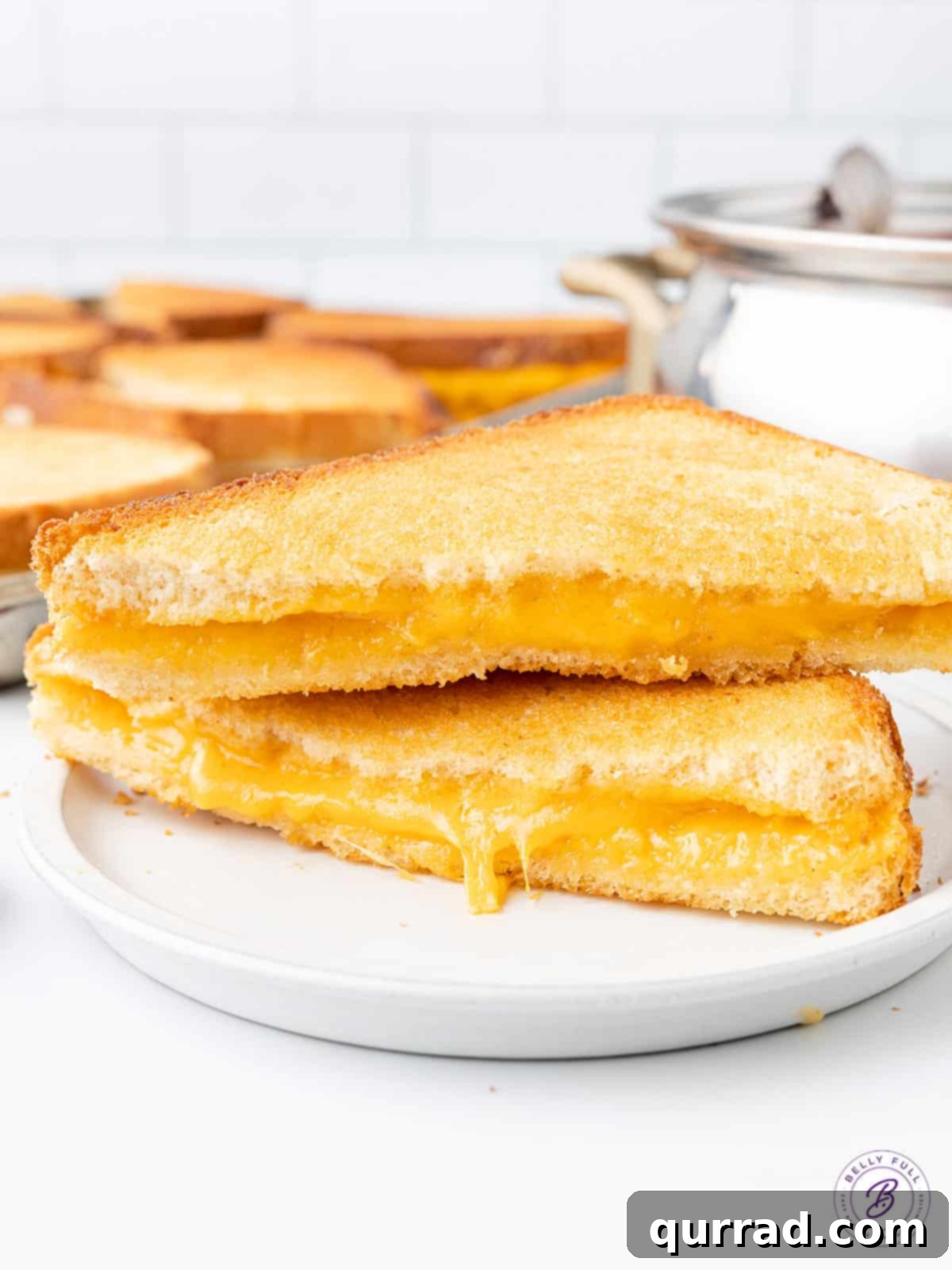 Two perfectly golden and melty halves of an oven grilled cheese sandwich on a white plate