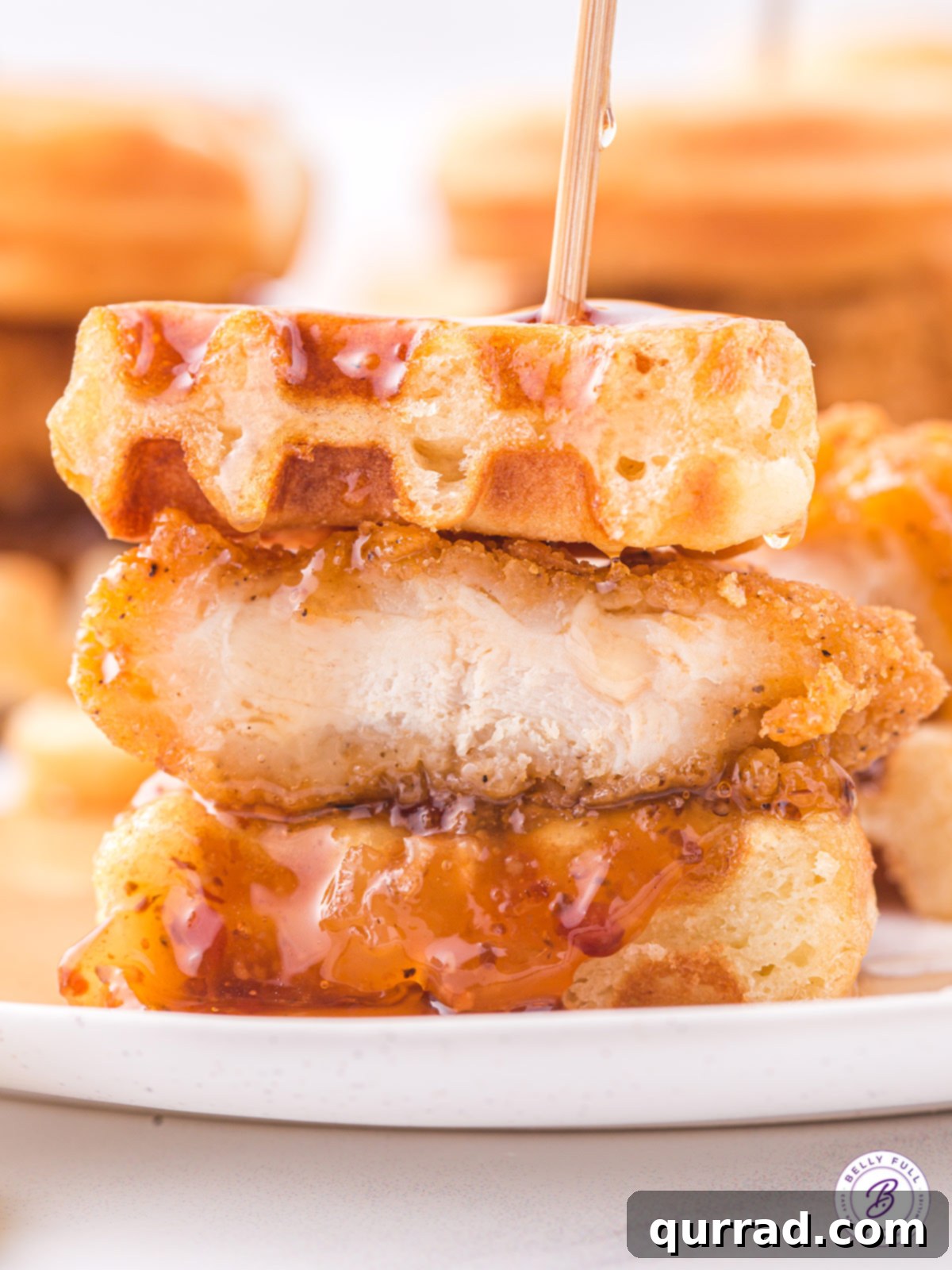 Enjoying a Chicken and Waffle Slider: A perfect bite. A chicken and waffle slider with a small bite taken out, revealing the layers inside.