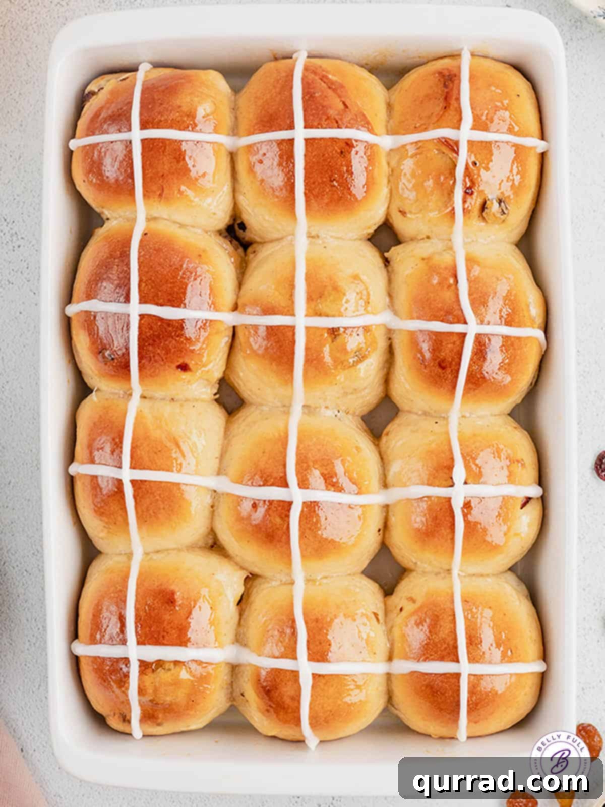 These soft and fluffy Hot Cross Buns are filled with plump juicy raisins, brushed with an orange glaze, and topped with a icing cross. Overhead view of a pan of hot cross buns