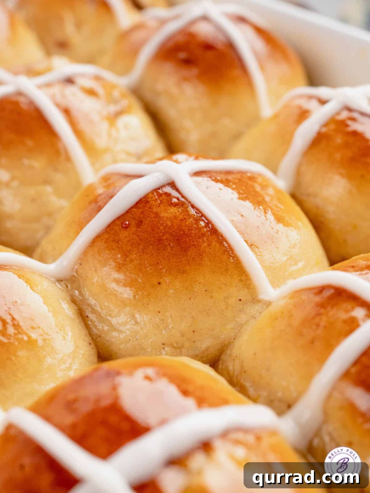 These soft and fluffy Hot Cross Buns are filled with plump juicy raisins, brushed with an orange glaze, and topped with a icing cross. Close up of Easter buns in a pan