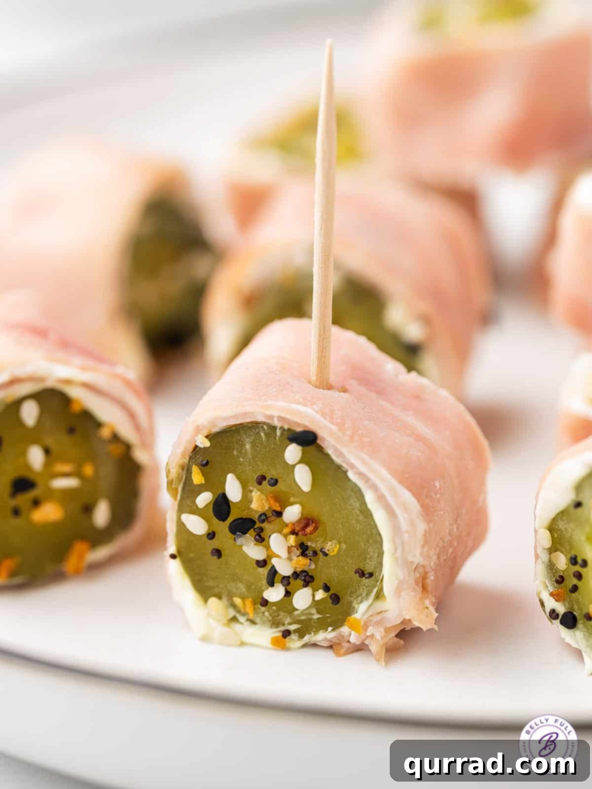 Ham Pickle Roll Ups are an easy and super delicious 3-ingredient snack or appetizer. Also referred to as Redneck Sushi, they're low carb! A dill pickle roll up with a toothpick on a plate, ready to be served as a low-carb appetizer.