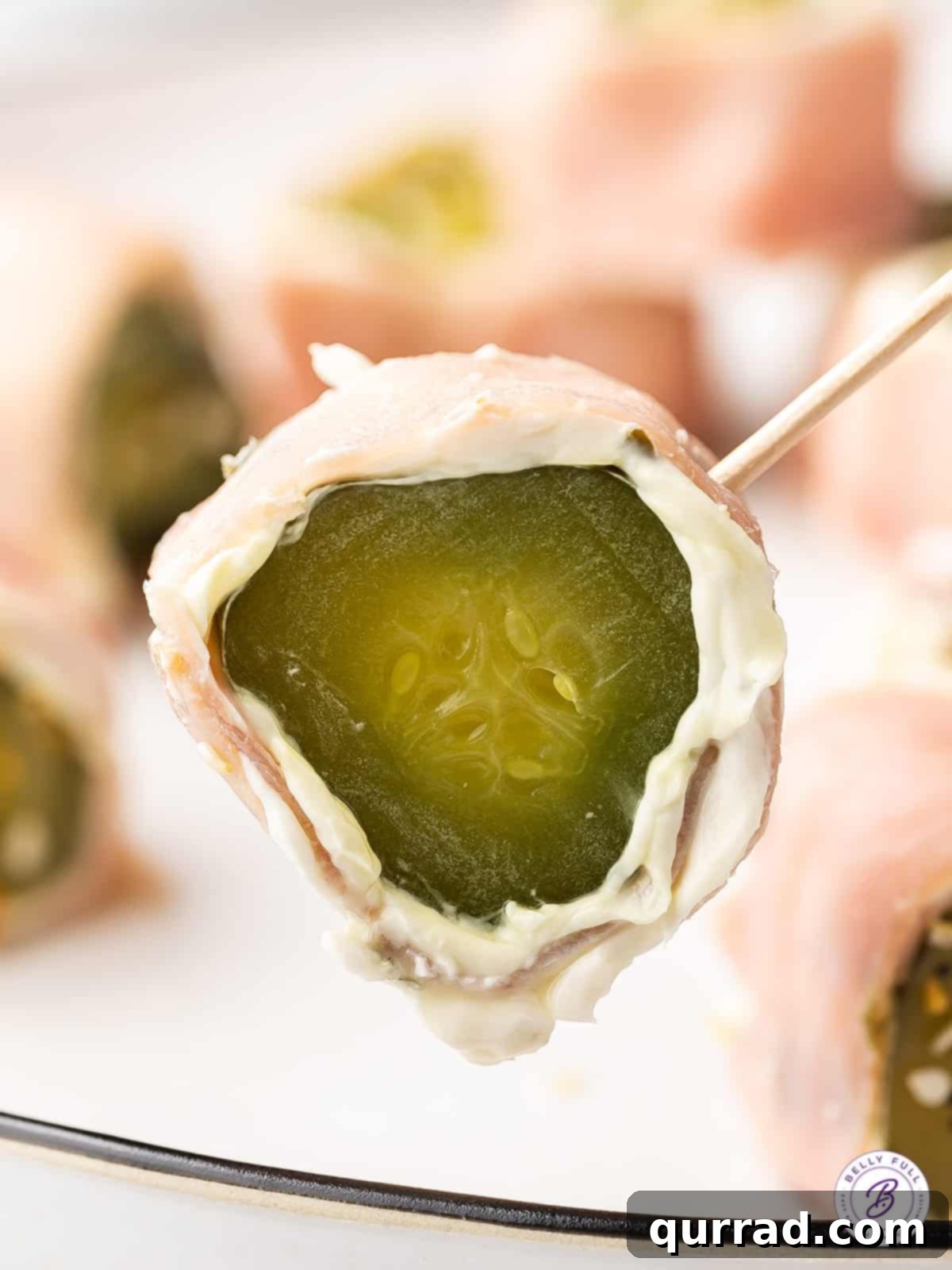 Ham Pickle Roll Ups are an easy and super delicious 3-ingredient snack or appetizer. Also referred to as Redneck Sushi, they're low carb! Close up shot of a single ham pickle roll up on a toothpick, highlighting its appealing layers and savory texture.