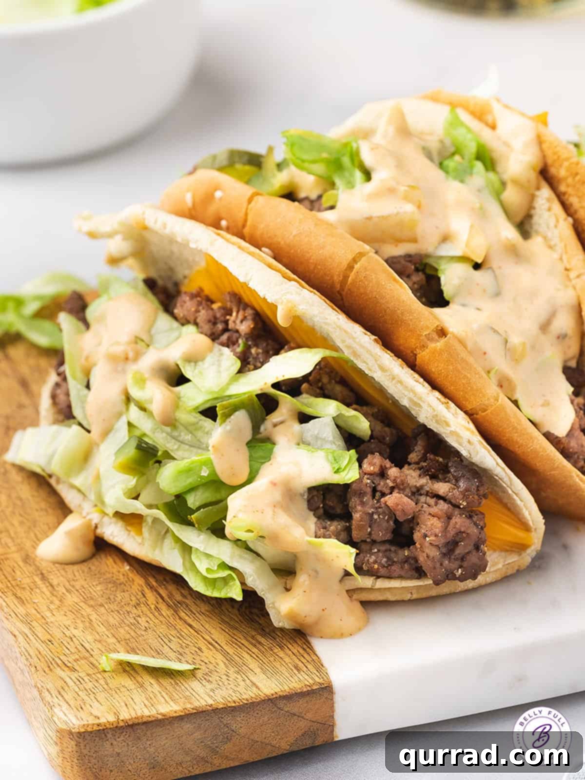 Delicious homemade Big Mac Tacos, ready to be enjoyed with fries and a shake. Two beautifully assembled Big Mac Tacos on a rustic wooden cutting board, garnished with fresh lettuce and pickles.