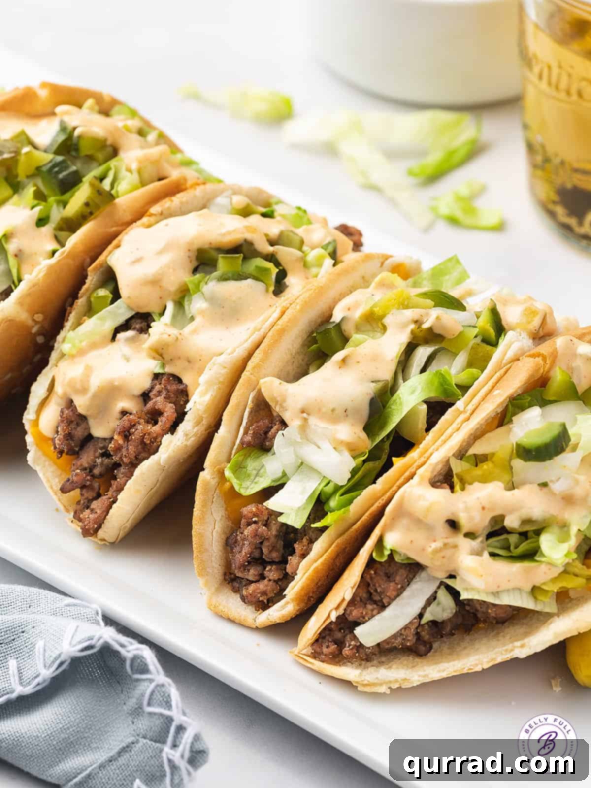 Irresistible burger tacos complete with all the essential Big Mac toppings and special sauce. Close-up overhead view of several Big Mac Tacos, generously topped with shredded lettuce, diced onions, pickles, and drizzled with the signature Big Mac dressing.