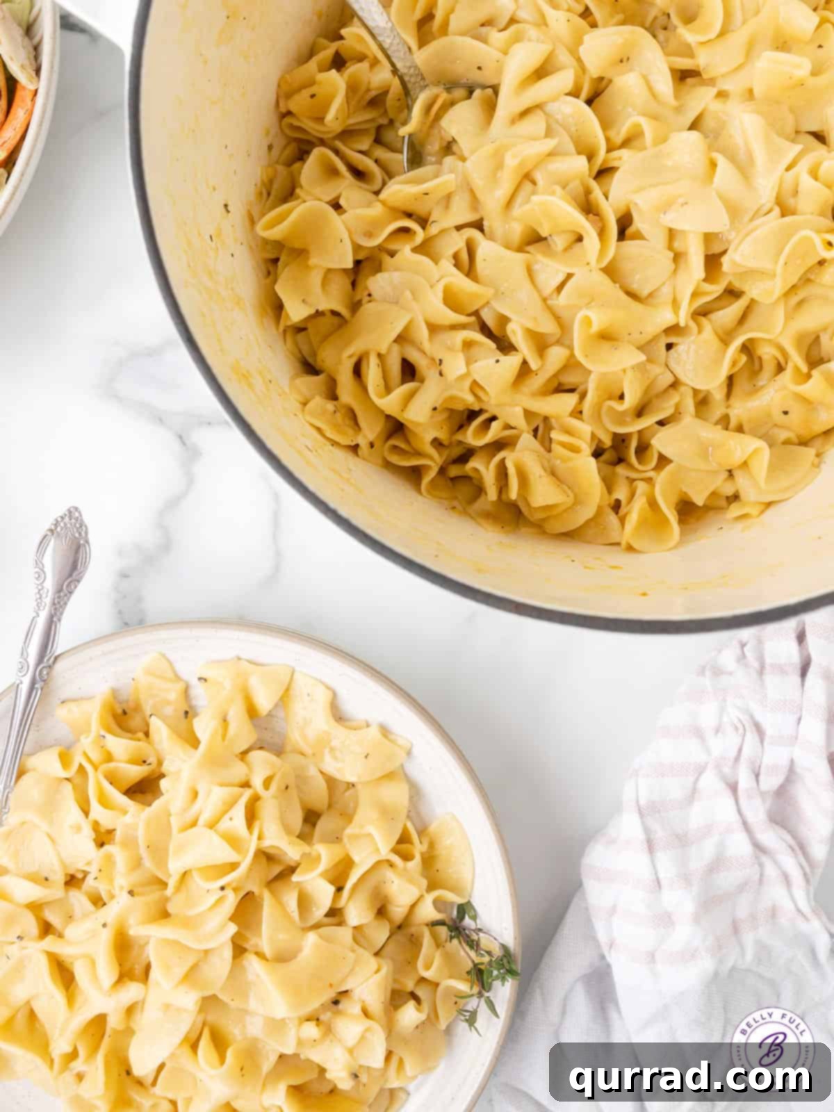 Cafeteria Noodles are a popular side dish made with egg noodles, cream of chicken soup, broth, and butter. Ready in 20 minutes! Overhead view of a pot of cafeteria noodles next to a ready plate, highlighting fresh butter