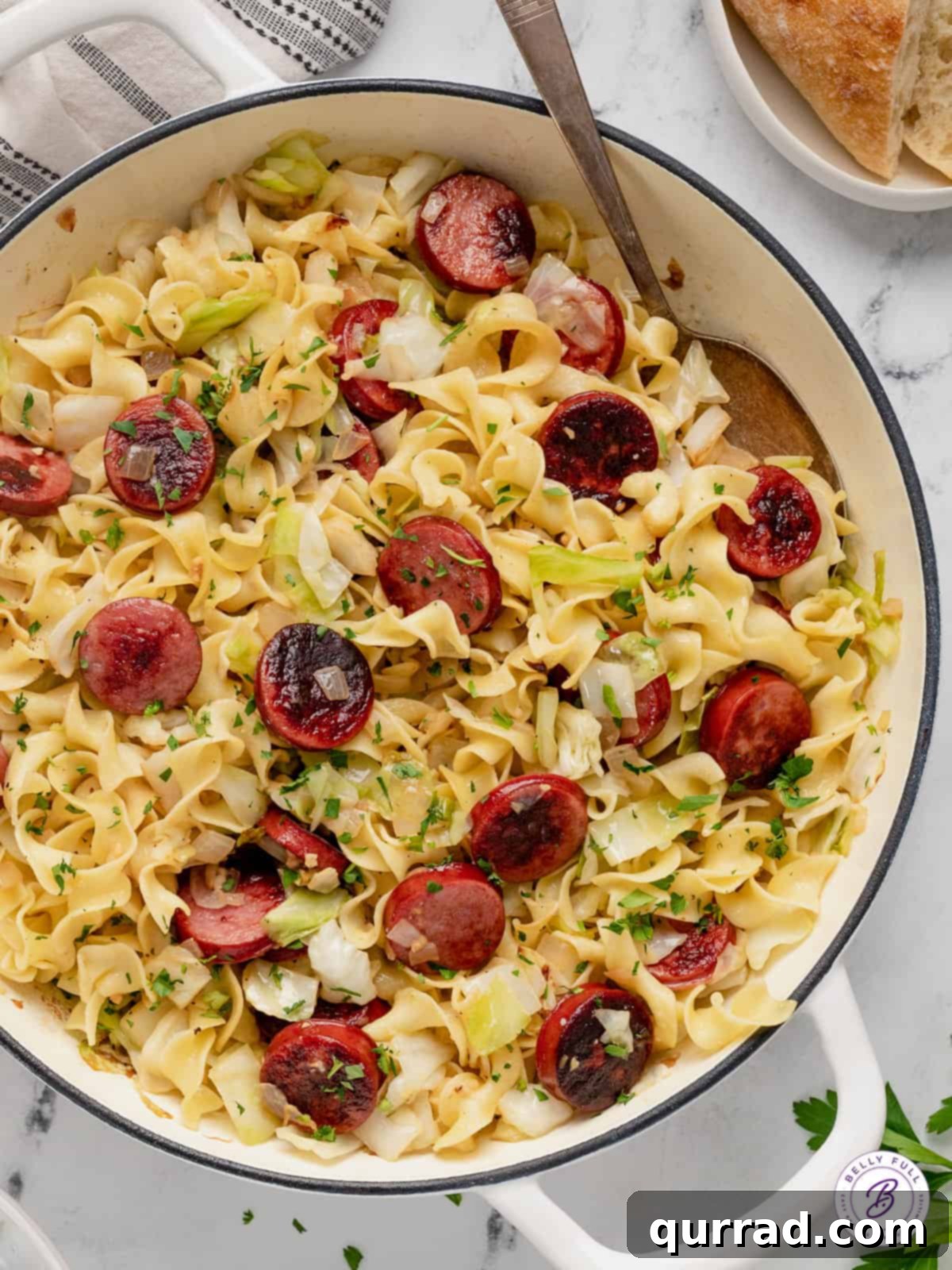 This Haluski recipe features fried cabbage and noodles with kielbasa and lots of butter. Savory, satisfying & ready in 30 minutes! A spoon in a pot of Polish haluski, showcasing the golden noodles and tender cabbage with pieces of kielbasa.