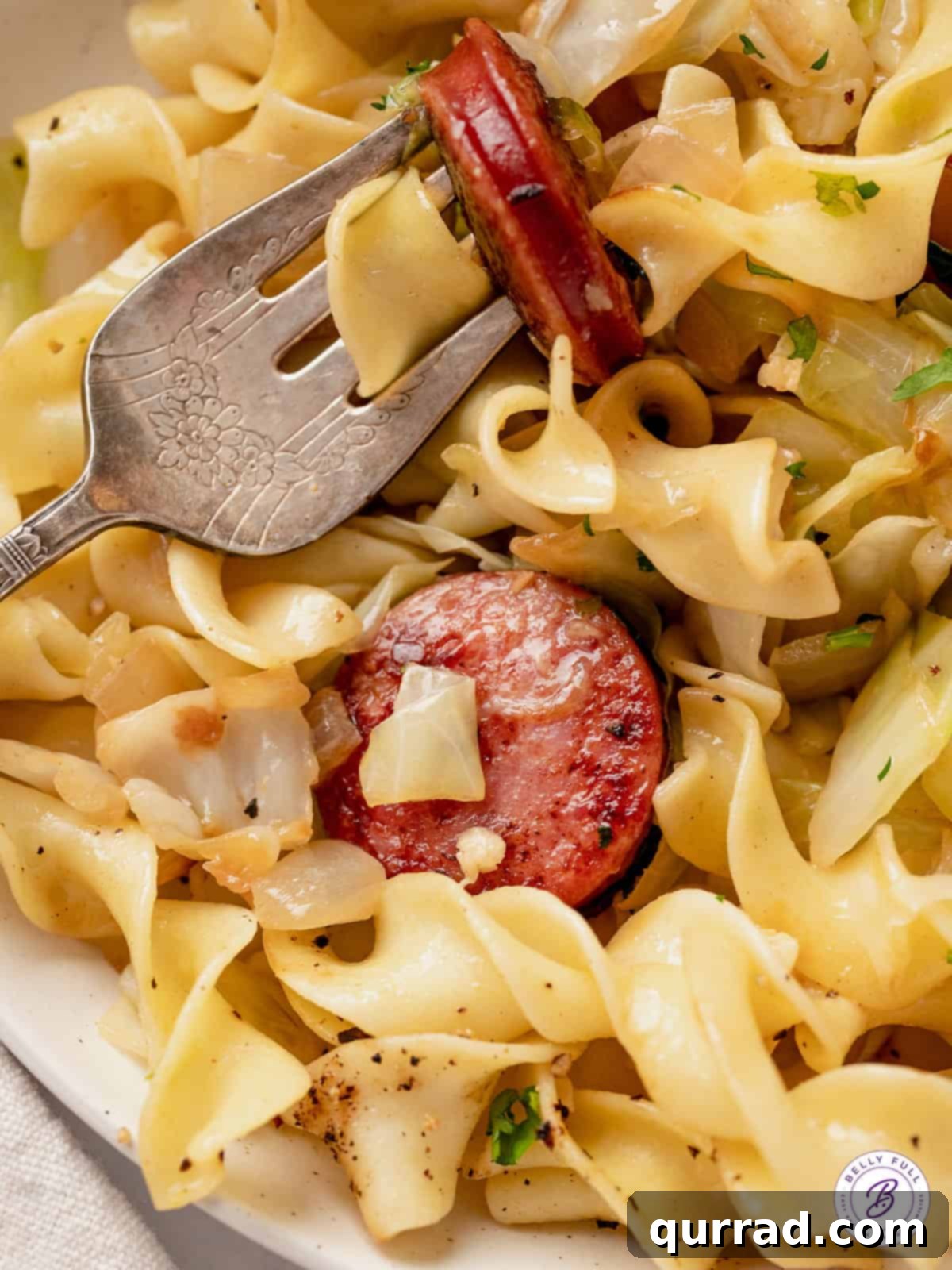 This Haluski recipe features fried cabbage and noodles with kielbasa and lots of butter. Savory, satisfying & ready in 30 minutes! Close up of fried cabbage and noodles with kielbasa, showing steam rising from the warm dish.