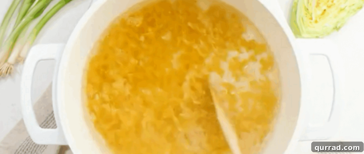 Hearty Haluski: Cabbage and Noodle Perfection 3 Cooking egg noodles in a white pot of boiling water, steam rising.