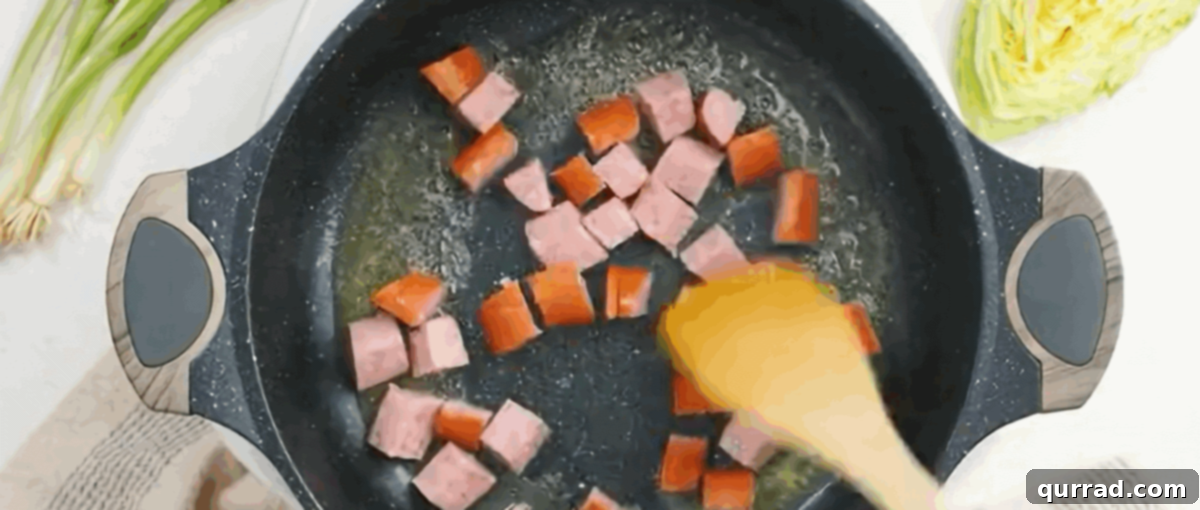 Hearty Haluski: Cabbage and Noodle Perfection 4 Sautéing sliced kielbasa sausage in a black skillet with melted butter.
