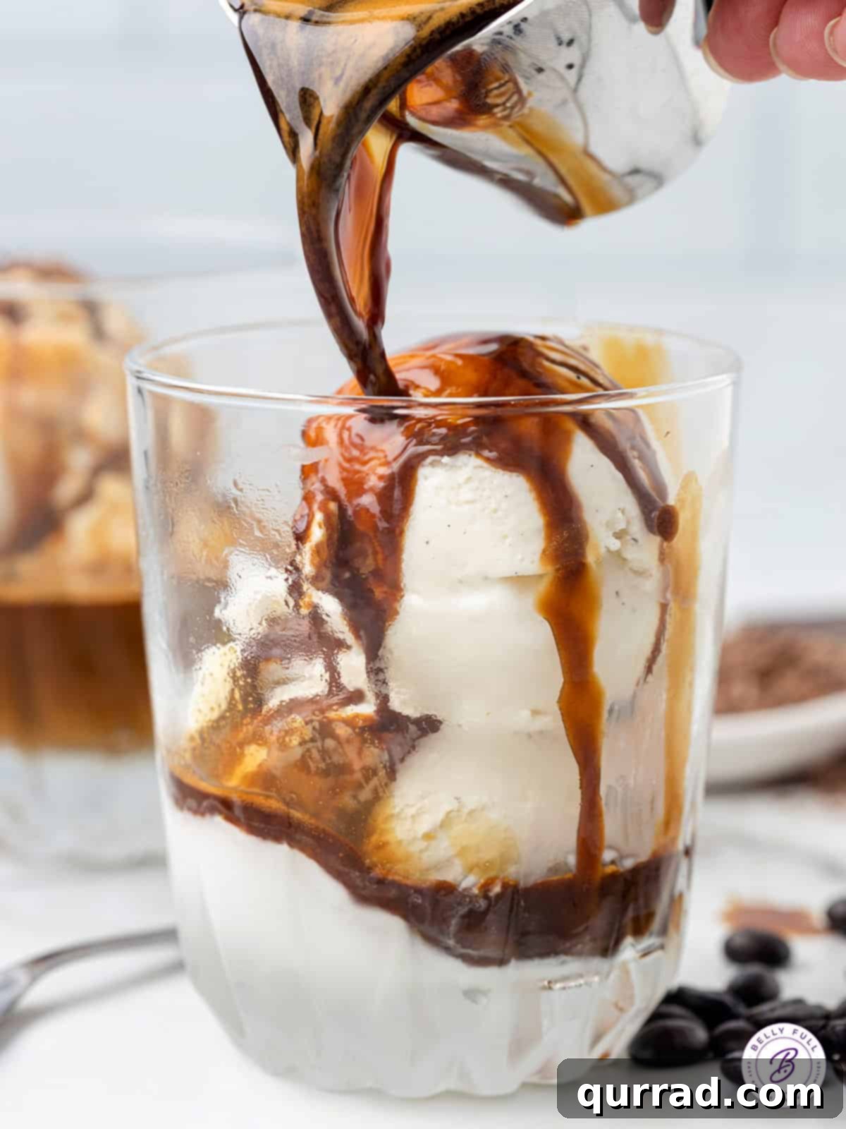 Make the perfect Affogato at home with just two ingredients - espresso and ice cream. Top with chocolate shavings for the perfect dessert. Hot espresso being poured over a scoop of vanilla ice cream in a clear glass, showing the melting process.