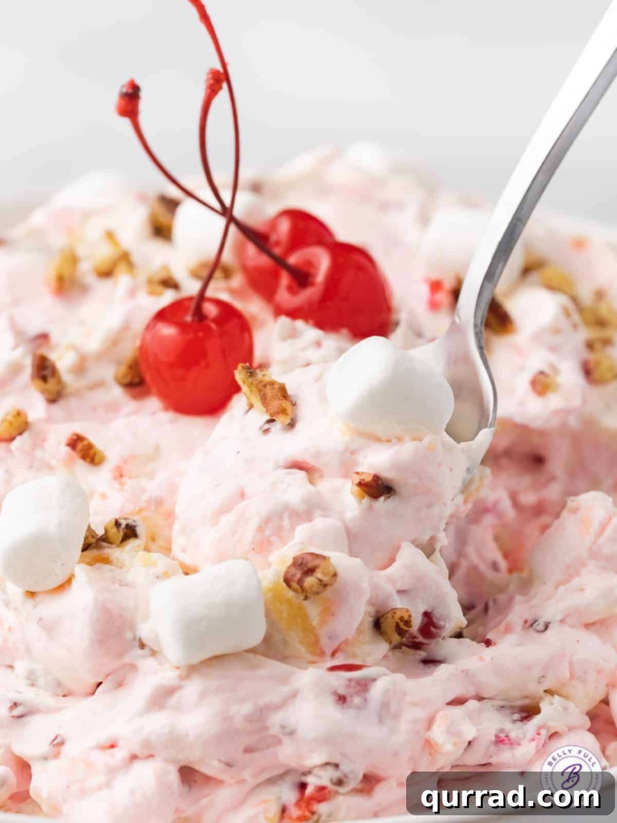 This Cherry Fluff is made with cream cheese, homemade whipped cream, maraschino cherries, and crushed pineapple for a quick and easy dessert. A spoon in a bowl of cherry fluff salad.