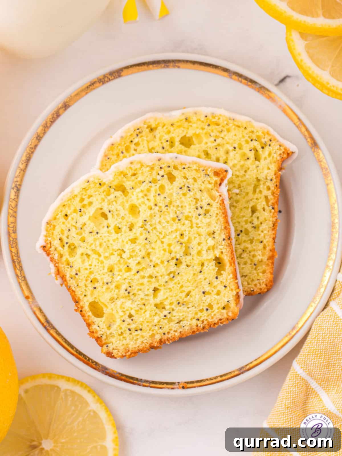 Two slices of lemon loaf on a plate with poppy seeds and zest