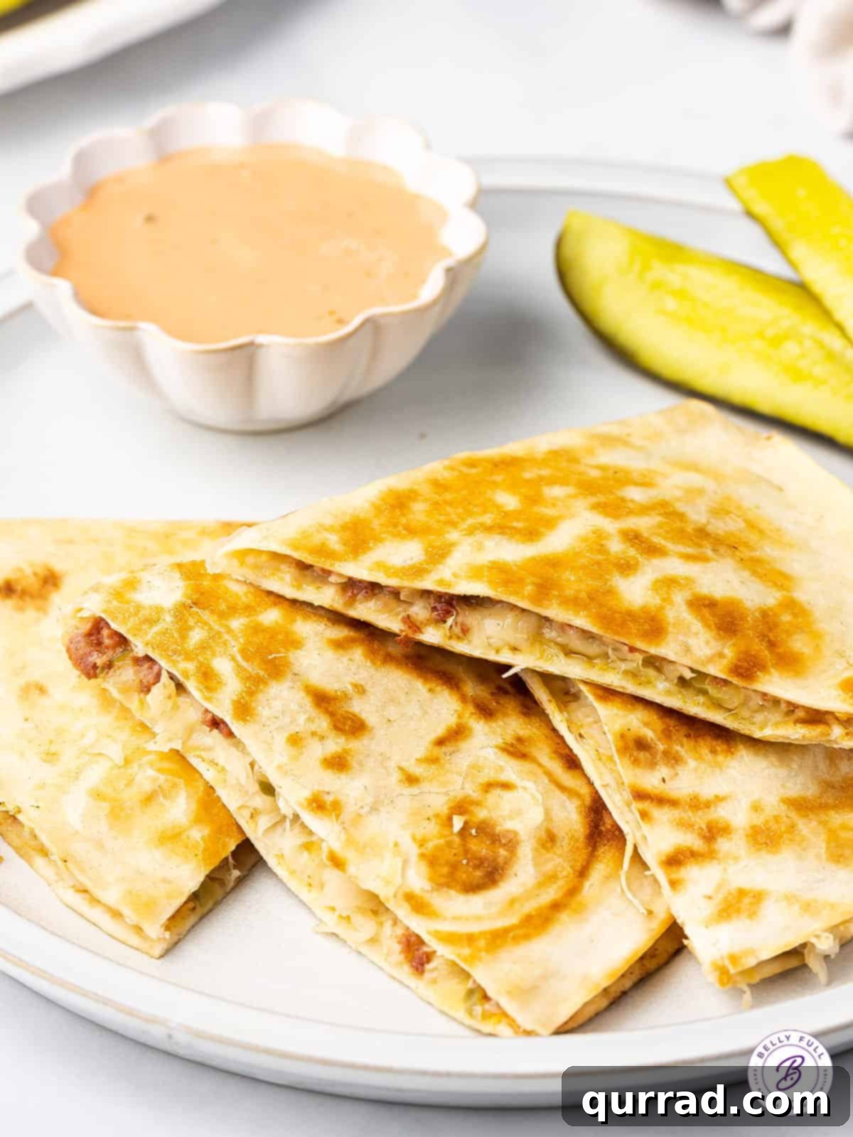 Reuben Quesadillas are loaded with corned beef, sauerkraut, Swiss cheese, and Thousand Island Dressing. Easy recipe for leftover corned beef! Slices of a corned beef quesadilla next to a little dish of thousand island dressing