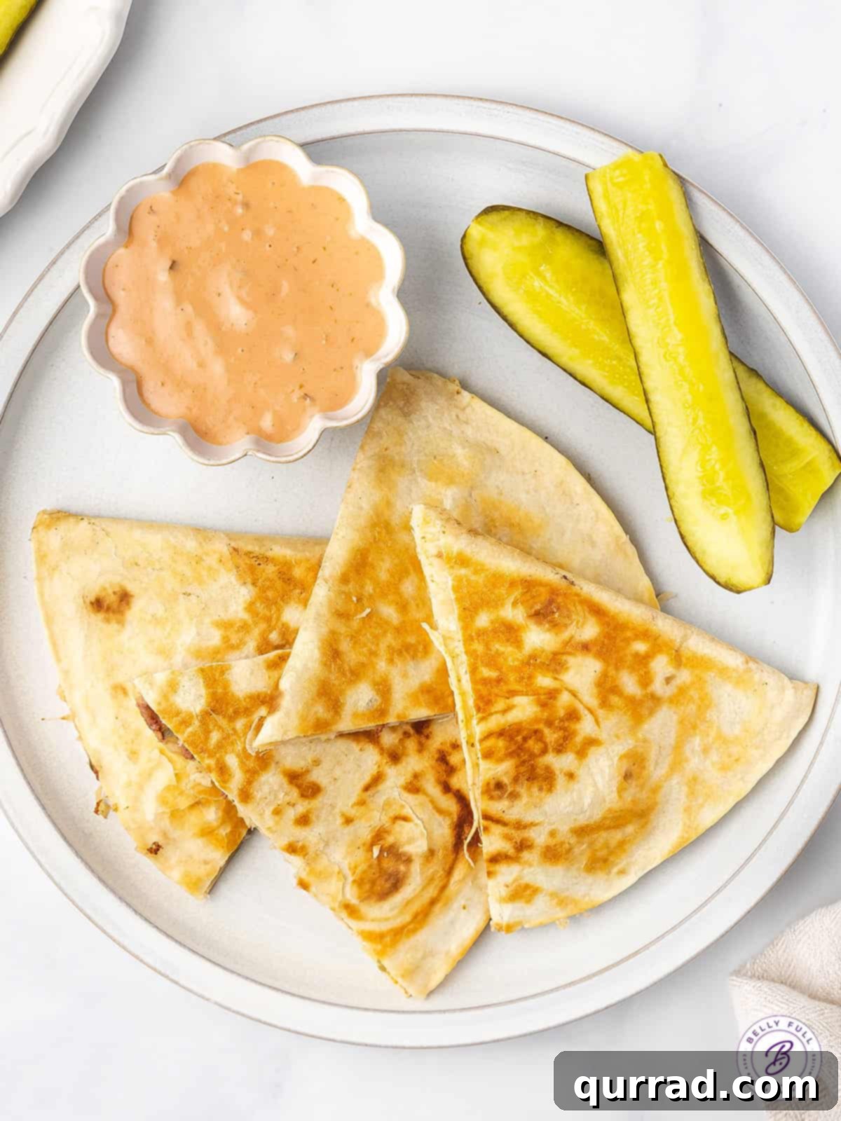 Reuben Quesadillas are loaded with corned beef, sauerkraut, Swiss cheese, and Thousand Island Dressing. Easy recipe for leftover corned beef! Overhead view of a sliced Reuben quesadilla with pickle spears on a plate