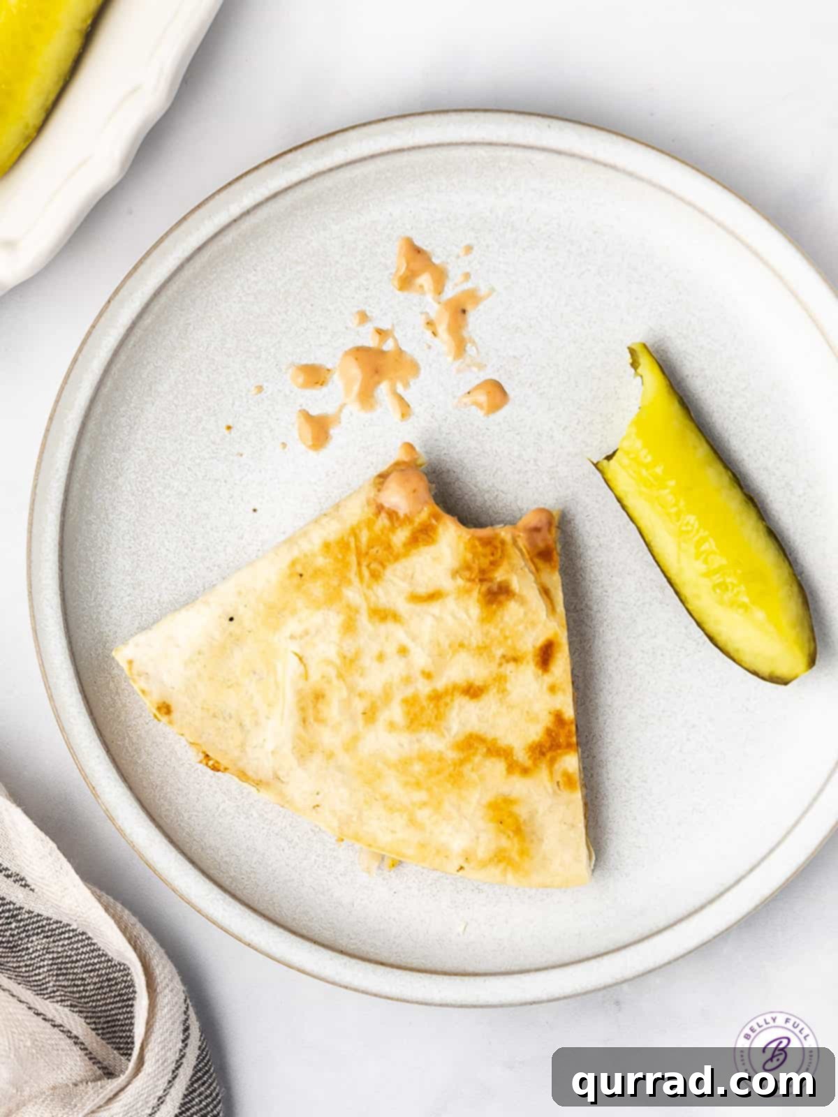Reuben Quesadillas are loaded with corned beef, sauerkraut, Swiss cheese, and Thousand Island Dressing. Easy recipe for leftover corned beef! A slice of a corned beef quesadilla, half eaten, with a pickle spread on a plate