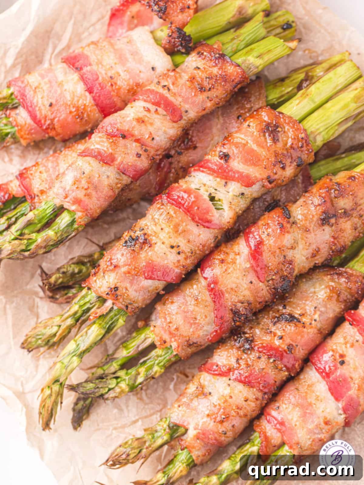 Delicious & Easy Air Fryer Bacon Wrapped Asparagus Overhead view of several bundles of air fried bacon wrapped asparagus on a white plate