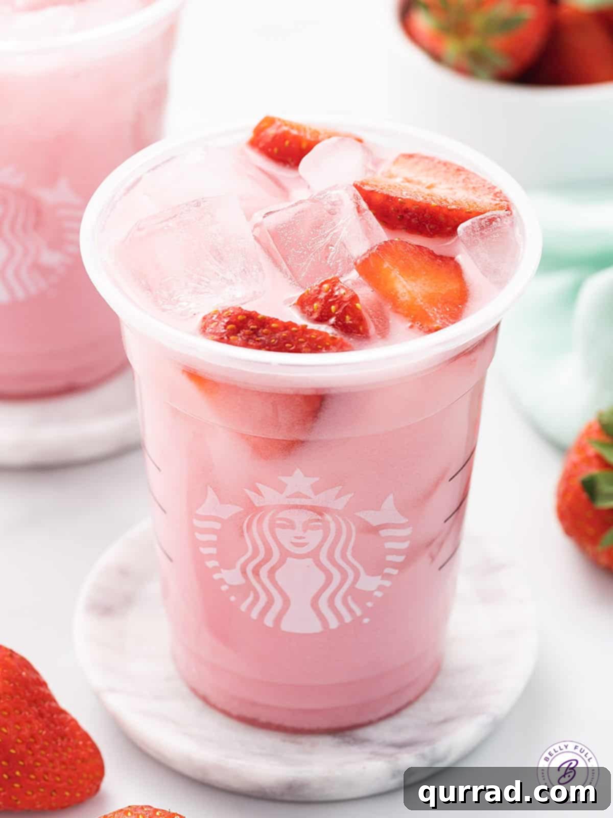 Enjoy a refreshing, dairy-free Starbucks Pink Drink copycat with this simple 3-ingredient recipe! Angled close-up view of a homemade Starbucks Pink Drink in a clear cup, garnished with strawberry slices and ready to drink.