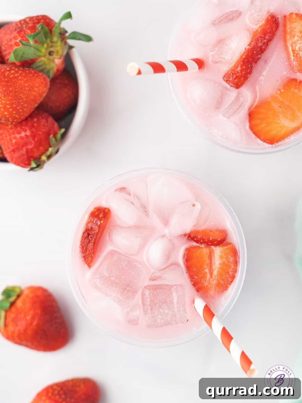 Recreate the popular Starbucks Pink Drink at home with this simple 3-ingredient, dairy-free recipe for a refreshing treat! Overhead shot of two homemade Starbucks Pink Drinks in clear cups, garnished with strawberry slices, sitting on a light surface.