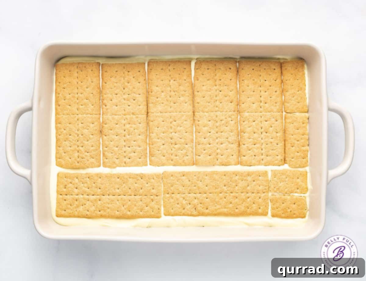 This Chocolate Eclair Dessert tastes like the best combination of Boston cream pie and a chocolate eclair. Just 5 ingredients! An overhead shot of graham crackers neatly arranged in the bottom of a 9x13 baking dish, forming the first layer of the no-bake eclair cake.