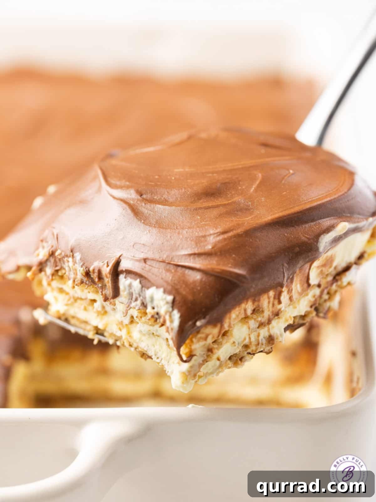 This Chocolate Eclair Dessert tastes like the best combination of Boston cream pie and a chocolate eclair. Just 5 ingredients! A spatula lifting a perfect square slice of Chocolate Eclair Cake from the dish, ready to be served, highlighting its soft, layered structure.