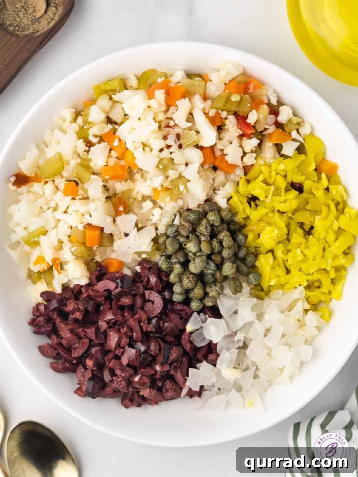 Precisely diced giardiniera, olives, pepperoncini, and marinated onions. Overhead view of finely diced olive salad ingredients in a bowl, ready to be mixed.