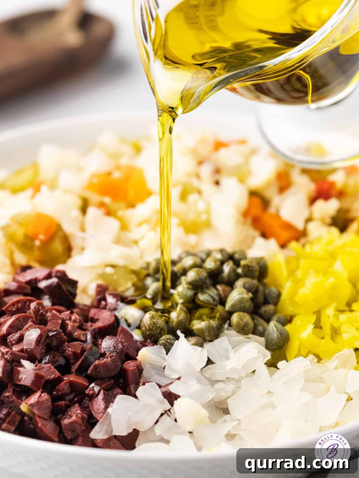 Ensure all ingredients are covered with oil for preservation. Olive oil being poured over olive salad ingredients.