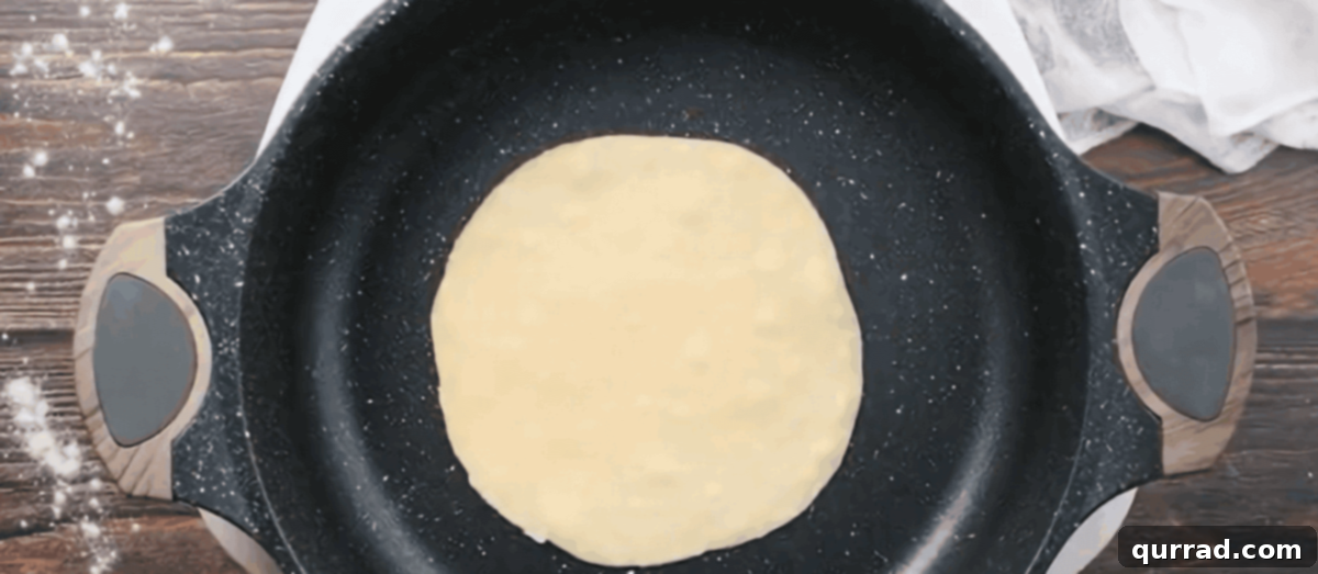 A homemade flour tortilla cooking in a hot skillet, with small bubbles starting to form on its surface.