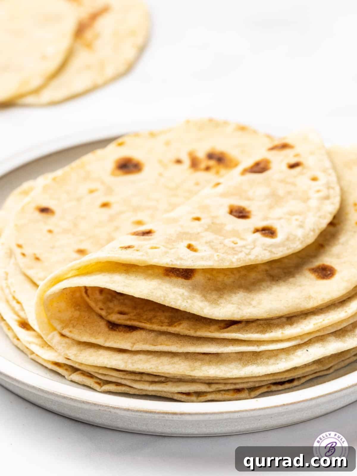 Freshly made, folded flour tortillas neatly stacked on a plate, ready for serving.