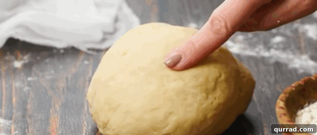 A finger pressing on a freshly kneaded dough ball to test its elasticity, indicating readiness for resting.