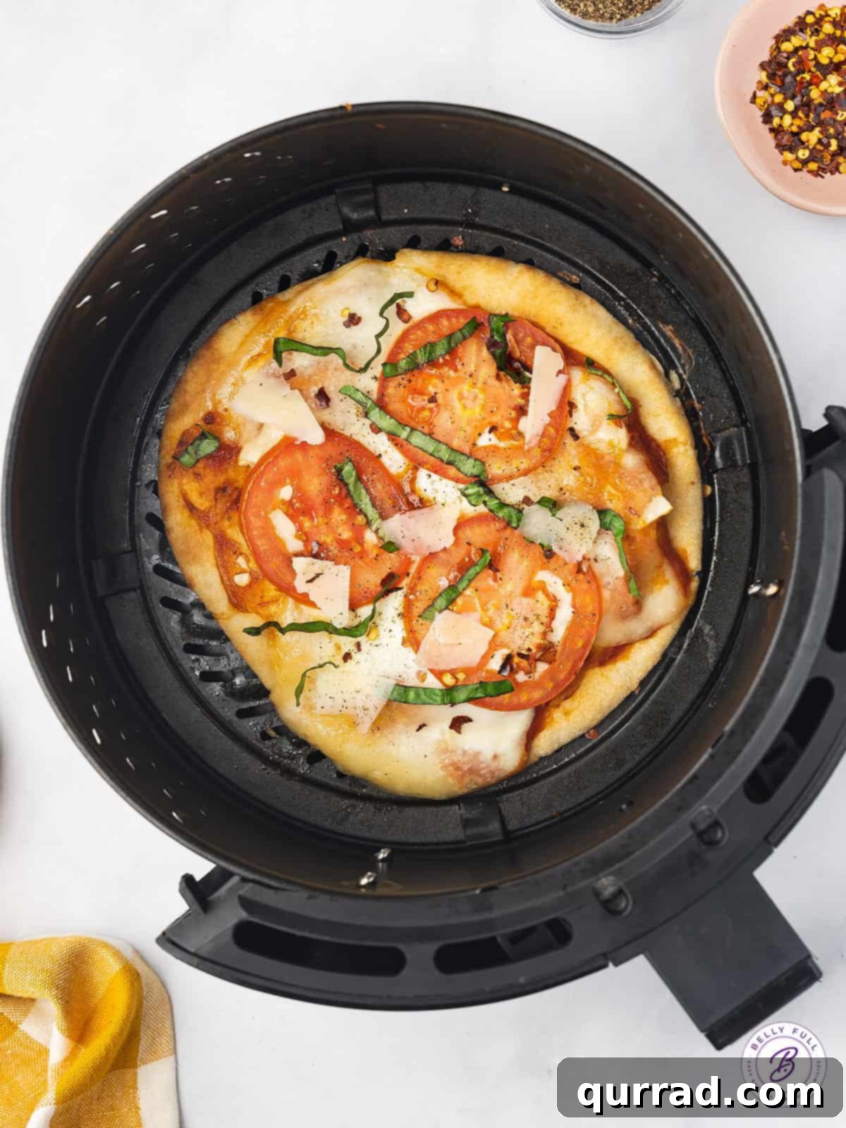 Watch your Air Fryer Margherita Pita Pizza become golden and bubbly. A margherita pizza cooking in the air fryer basket, with melted cheese and bubbling sauce.