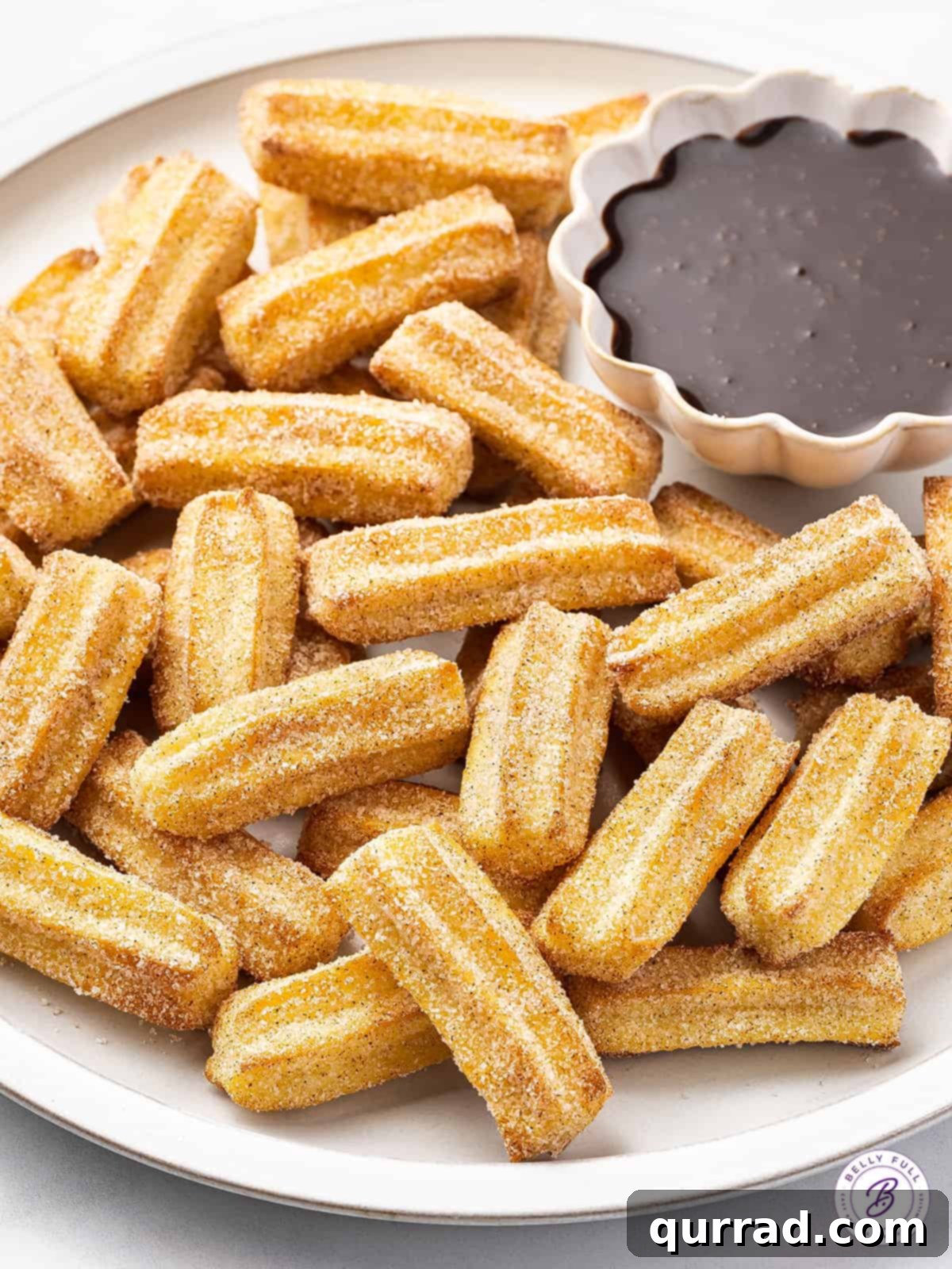 Easy Air Fryer Churro Bites: Crispy, tender, and no oil needed! Overhead view of a plate of air fryer churro bites with a dish of chocolate sauce for dipping